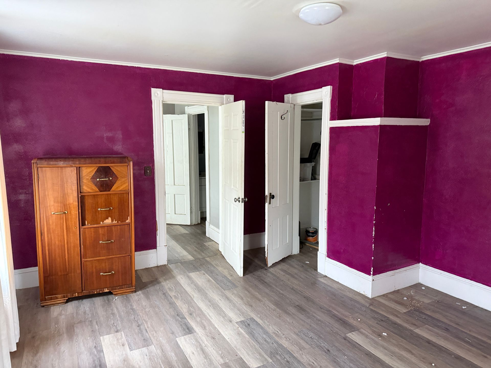 Empty room with purple walls, gray wood floor, white trim, and open closet doors