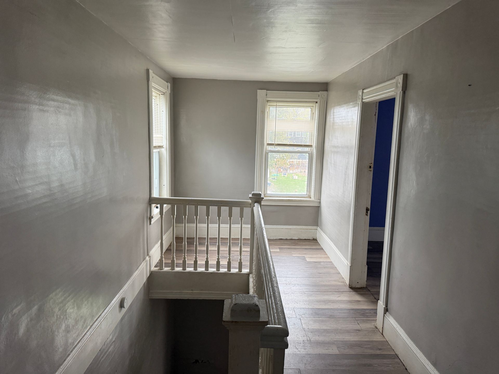 Narrow upstairs hallway with white walls, banister, and windows at the end.