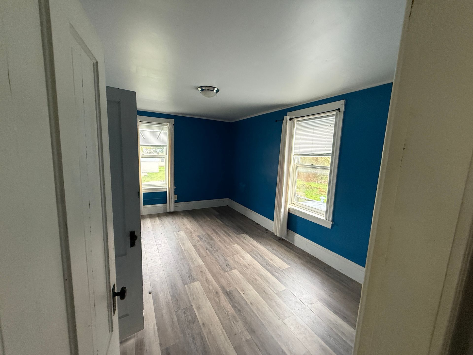 Empty room with blue walls, gray wood flooring, and two windows letting in daylight