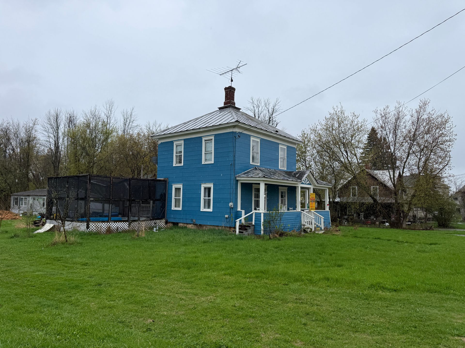 Blue two-story house with white trim on a grassy lot under a cloudy sky