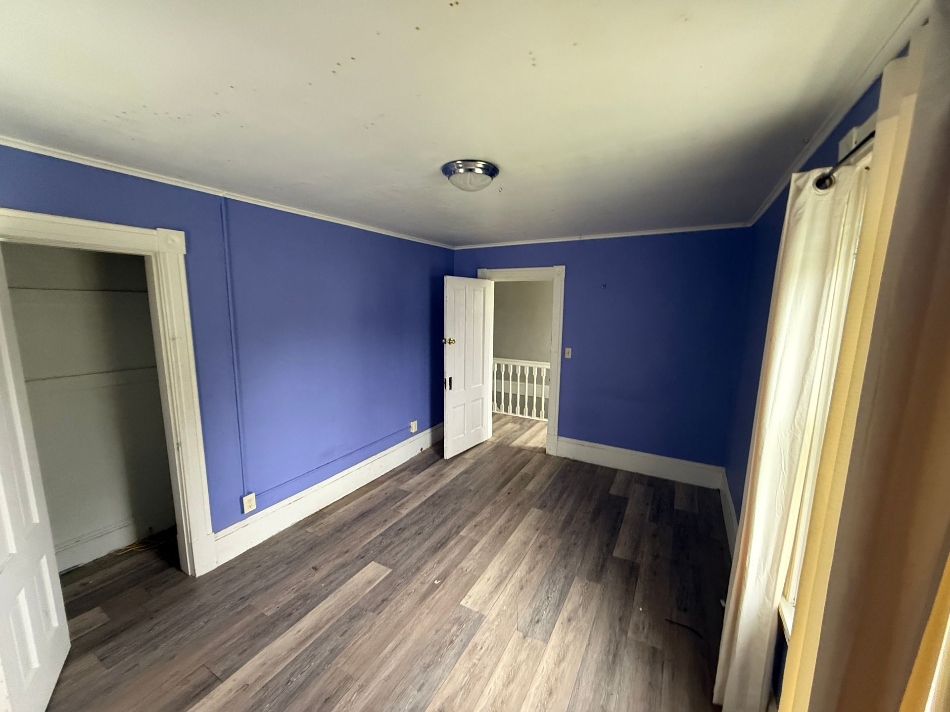 Empty bedroom with blue walls, gray wood flooring, and white trim, seen from an open doorway.