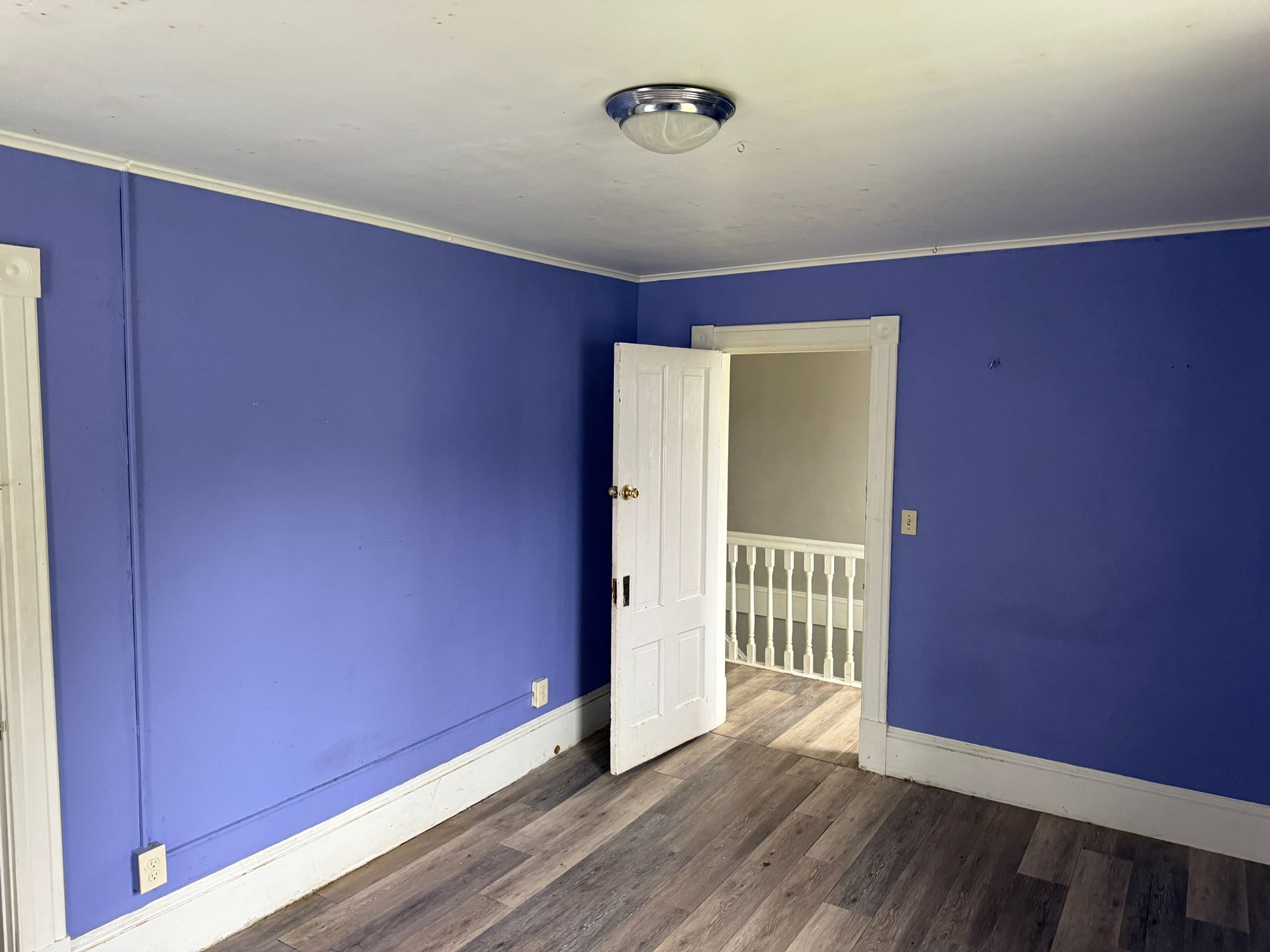 Empty room with bright blue walls, white trim, open door, and wood-look flooring
