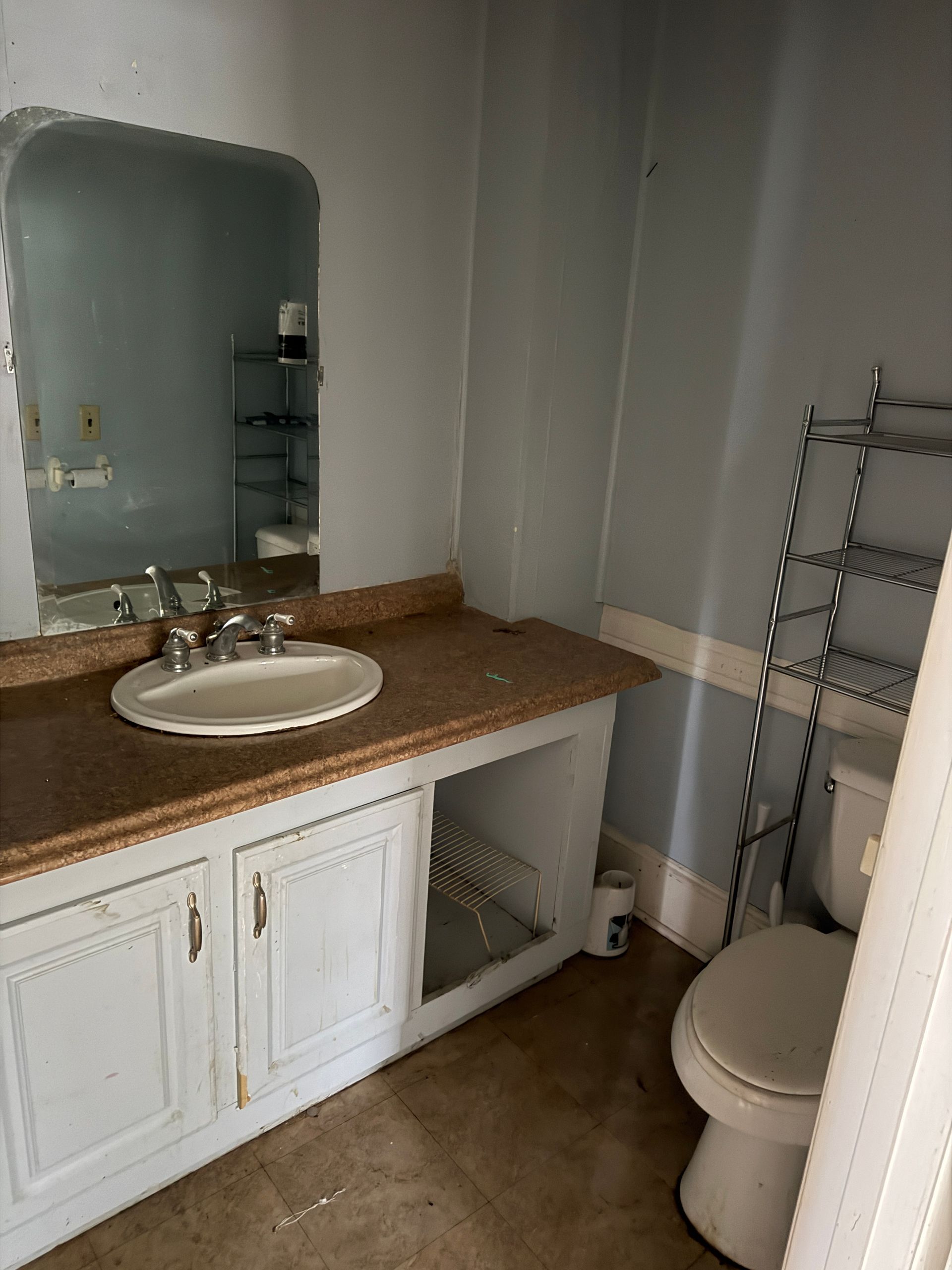 Small bathroom with white vanity, brown countertop, round sink, mirror, towel rack, and toilet.