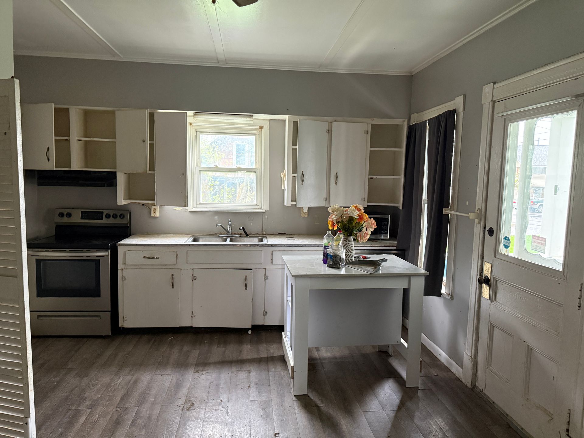 Bright kitchen with white cabinets, stove, island, and open door to the outside.