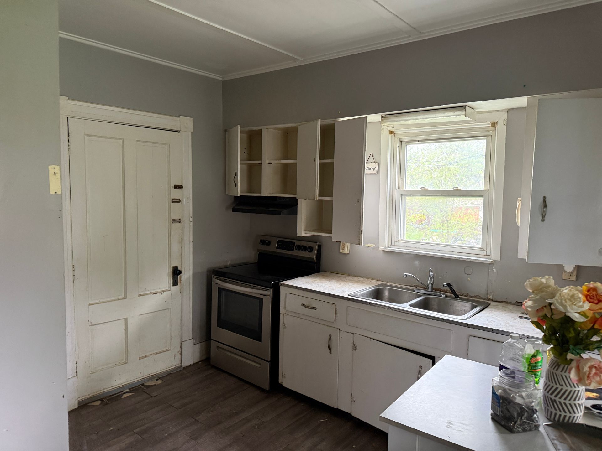 Kitchen with gray walls, white cabinets, stove, sink under a window, and a countertop with flowers.