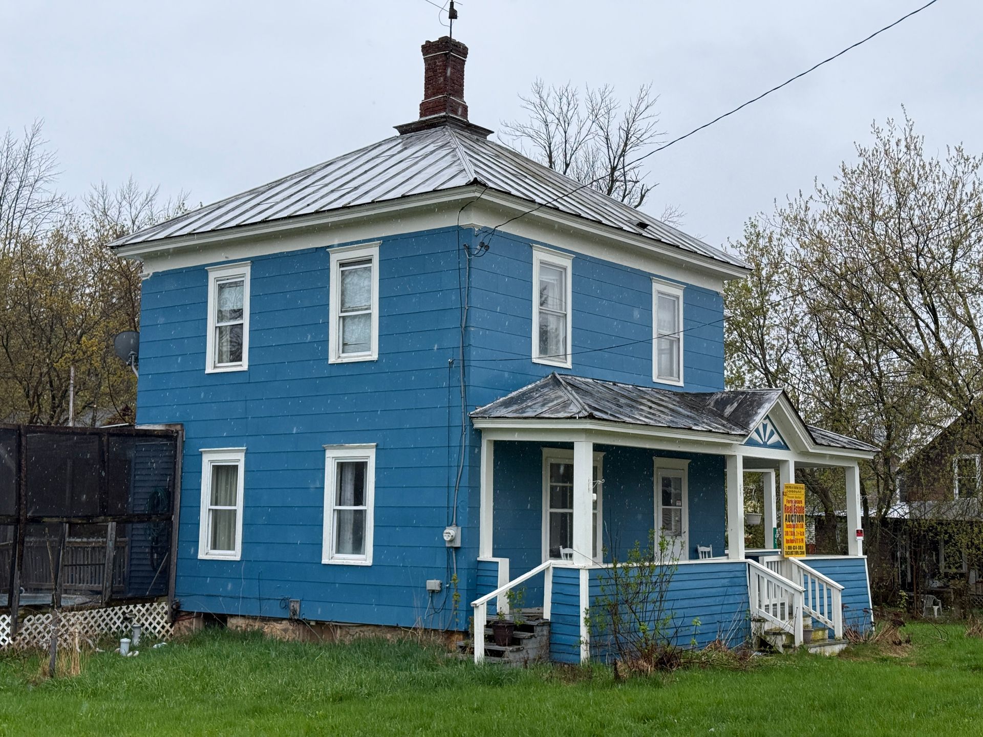 Blue two-story house with white trim and a small front porch in a leafy yard