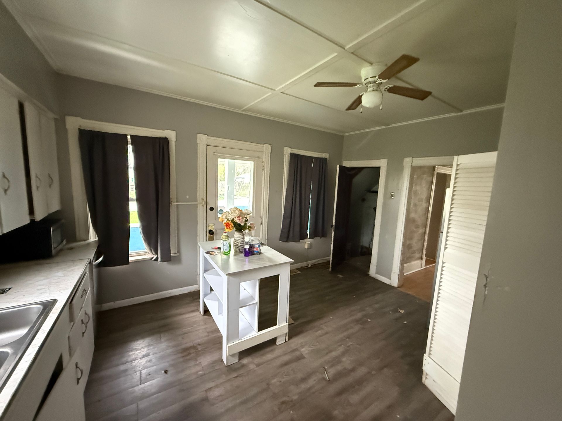 Small gray room with wood floor, central table with flowers, windows, ceiling fan, and open doorways