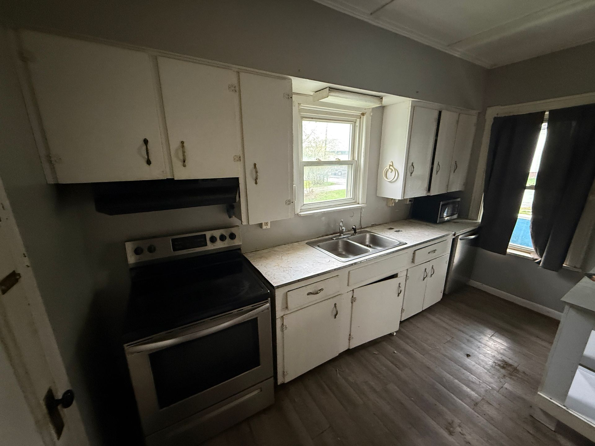 Small kitchen with white cabinets, black stove, sink by window, and gray wood-style floor.