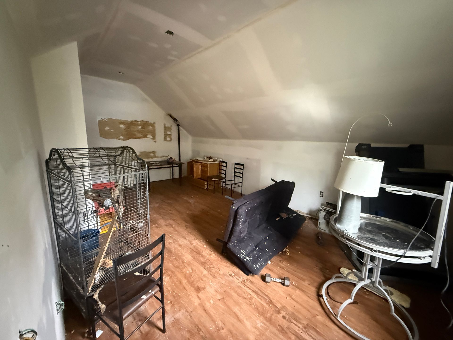 Attic room with wood floor, chairs, a lamp, and a black TV on a stand.
