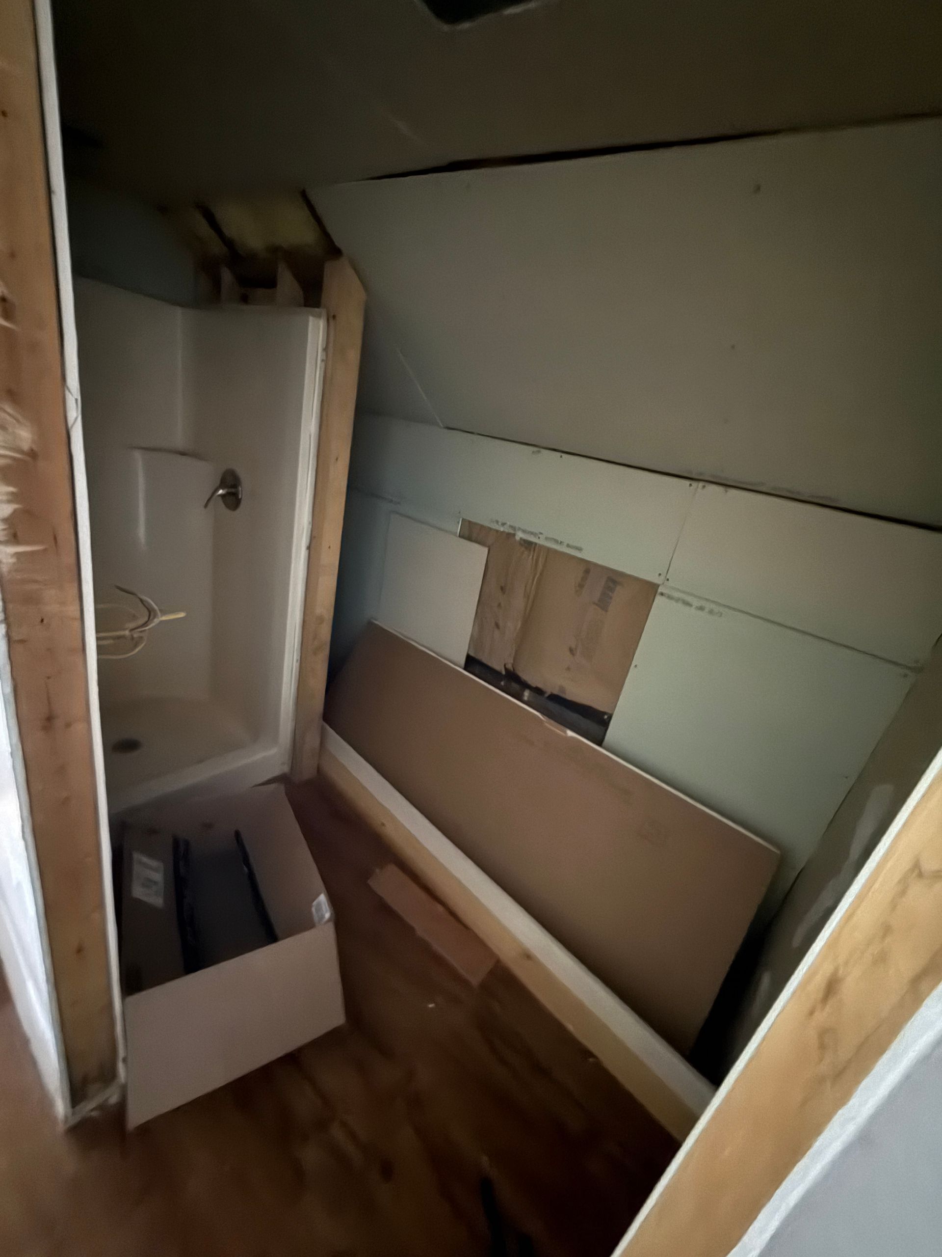Partially renovated bathroom with stacked drywall panels, a shower stall, and wood flooring