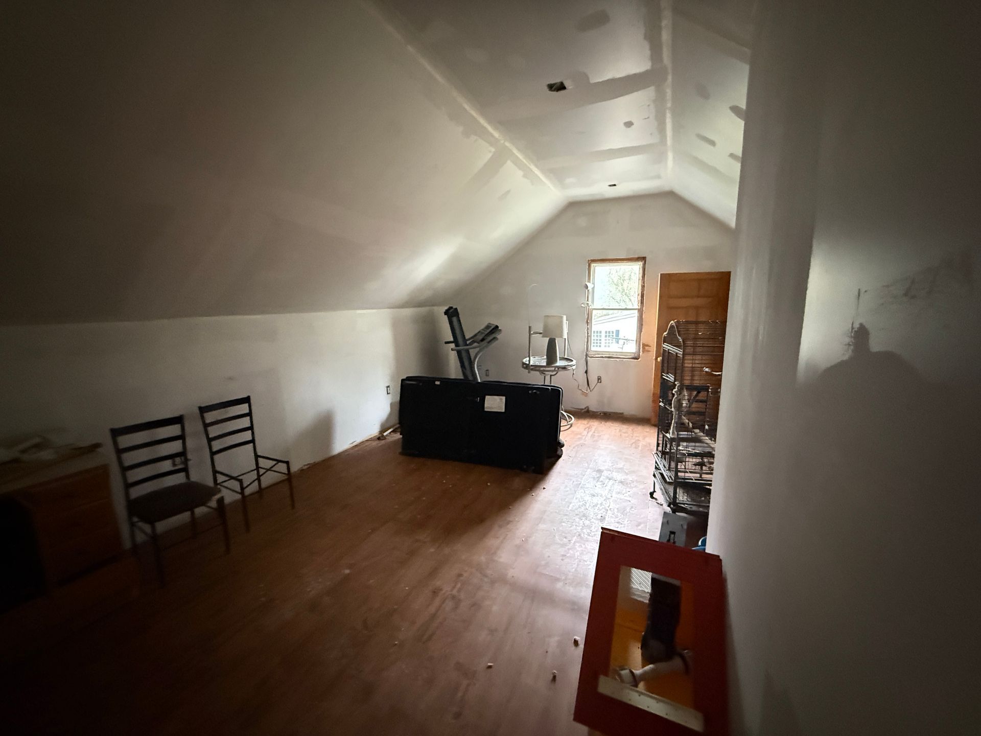 Small attic room with wood floor, a black desk, chairs, and a window at the far end.