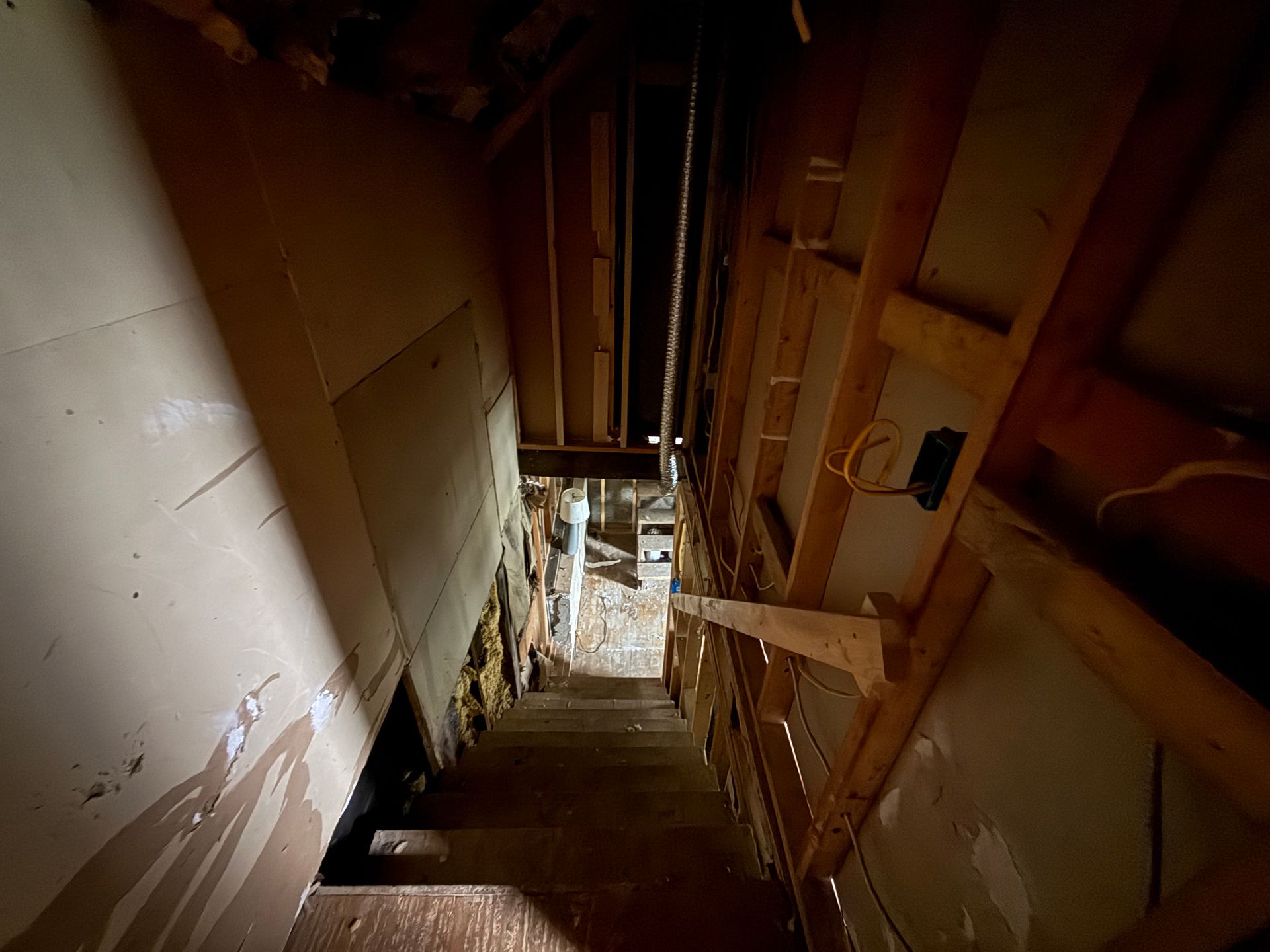 Narrow unfinished stairwell with exposed wooden framing and a walkway below