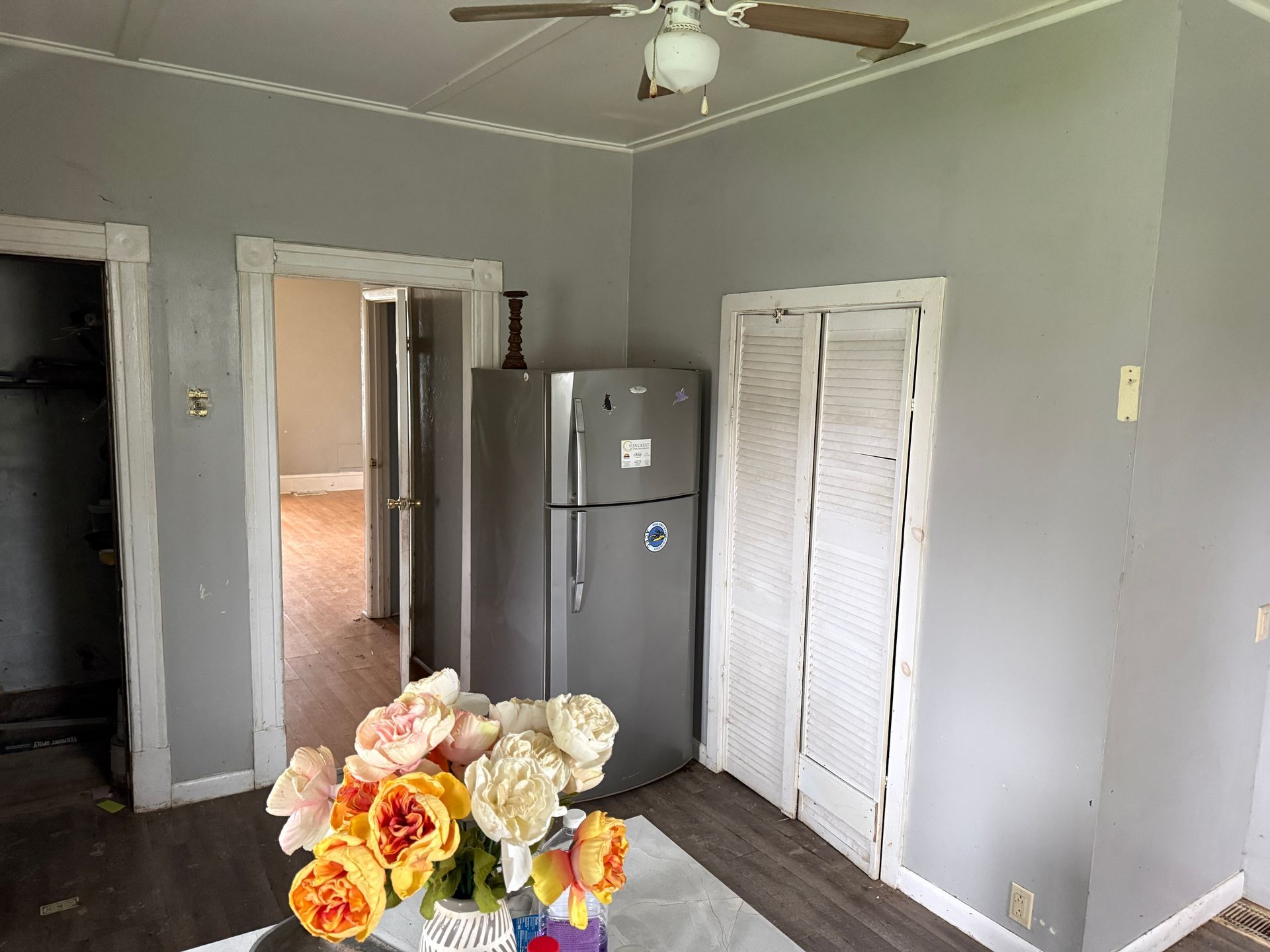 Small kitchen with gray walls, a stainless fridge, white closet doors, and flowers in the foreground.