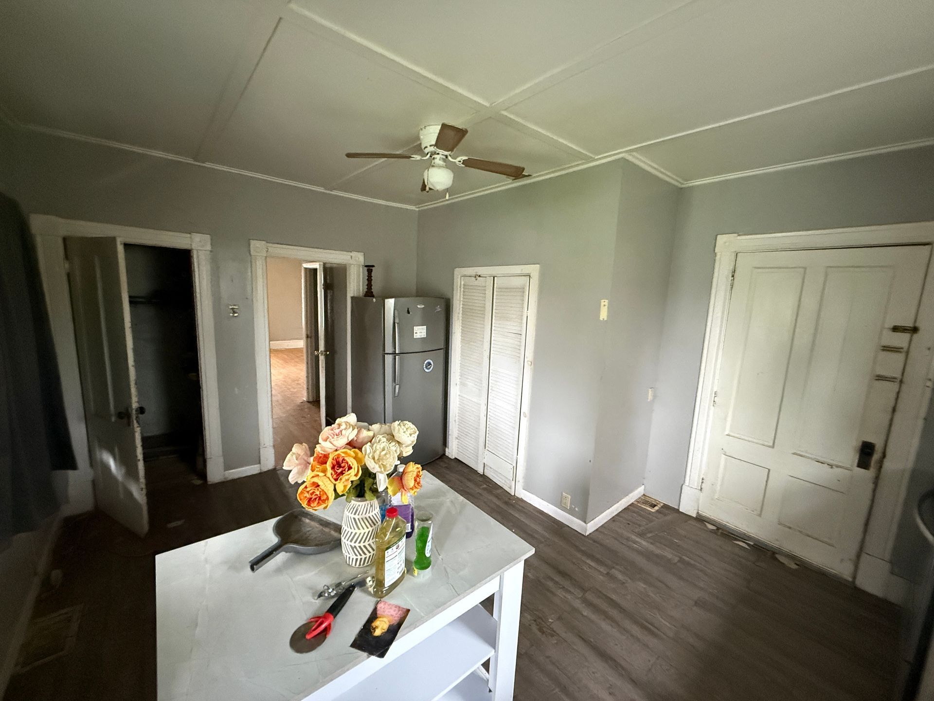 Empty gray room with ceiling fan, white doors, dark flooring, and a table with flowers in the foreground
