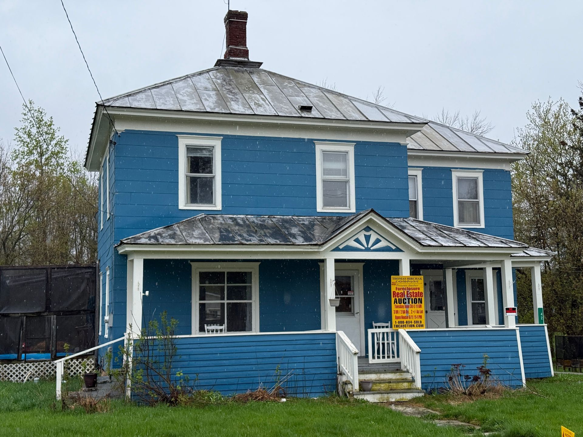 Blue two-story house with a front porch and a yellow sign in the yard