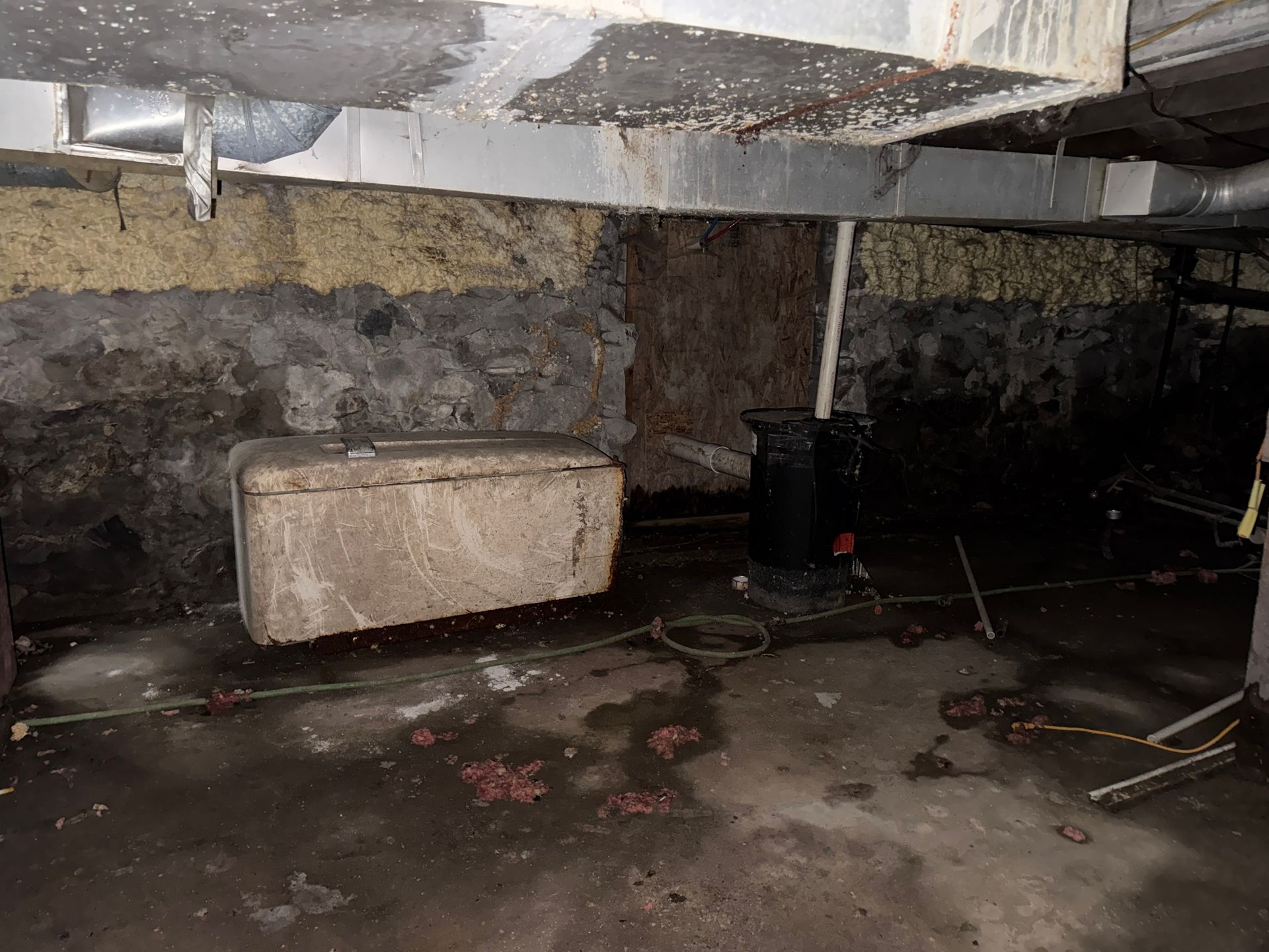 Basement crawlspace with concrete floor, stone wall, low beams, and a rectangular concrete block.