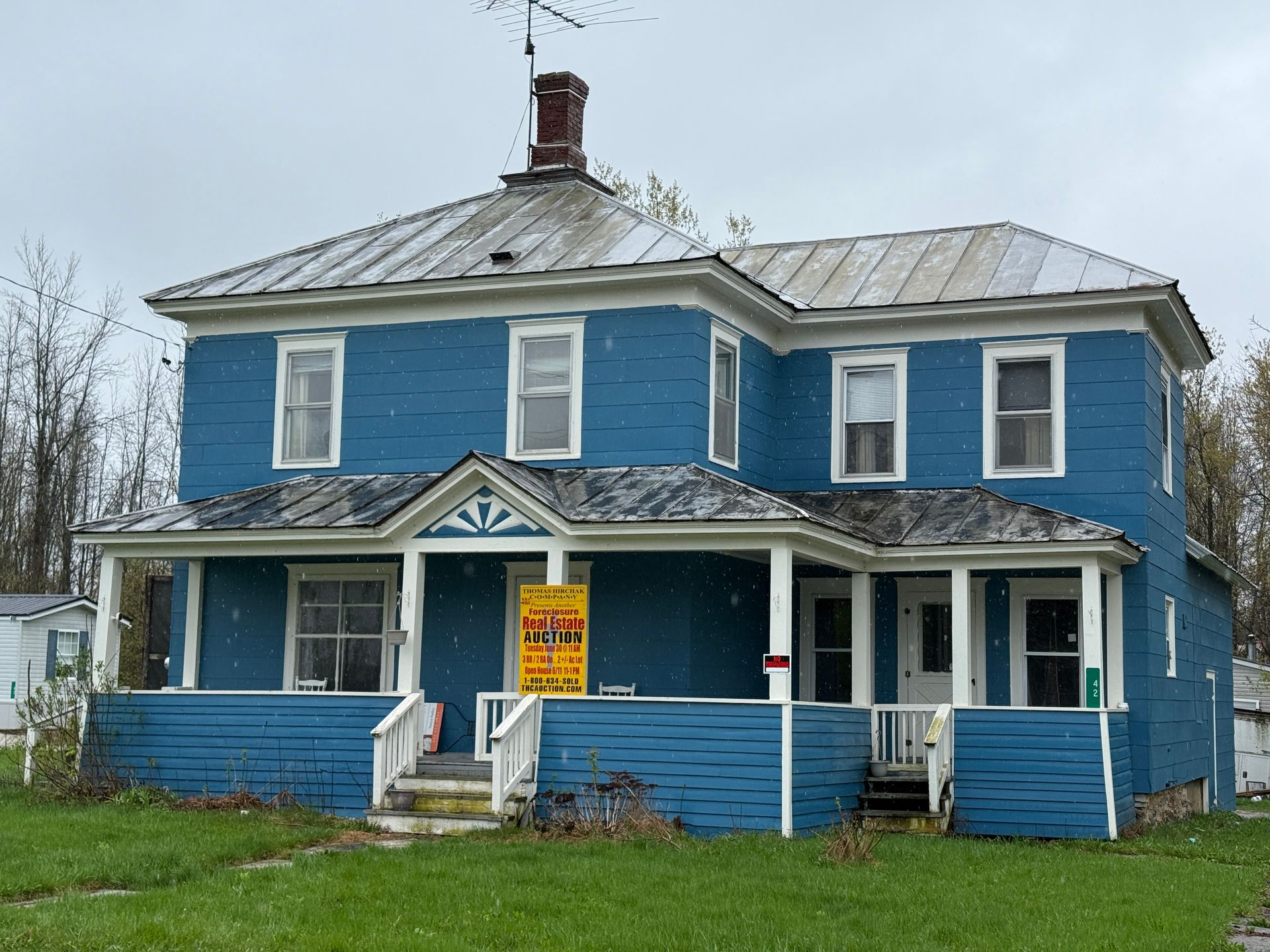 Blue two-story house with paint and a front porch, with a yellow for-sale sign in front.