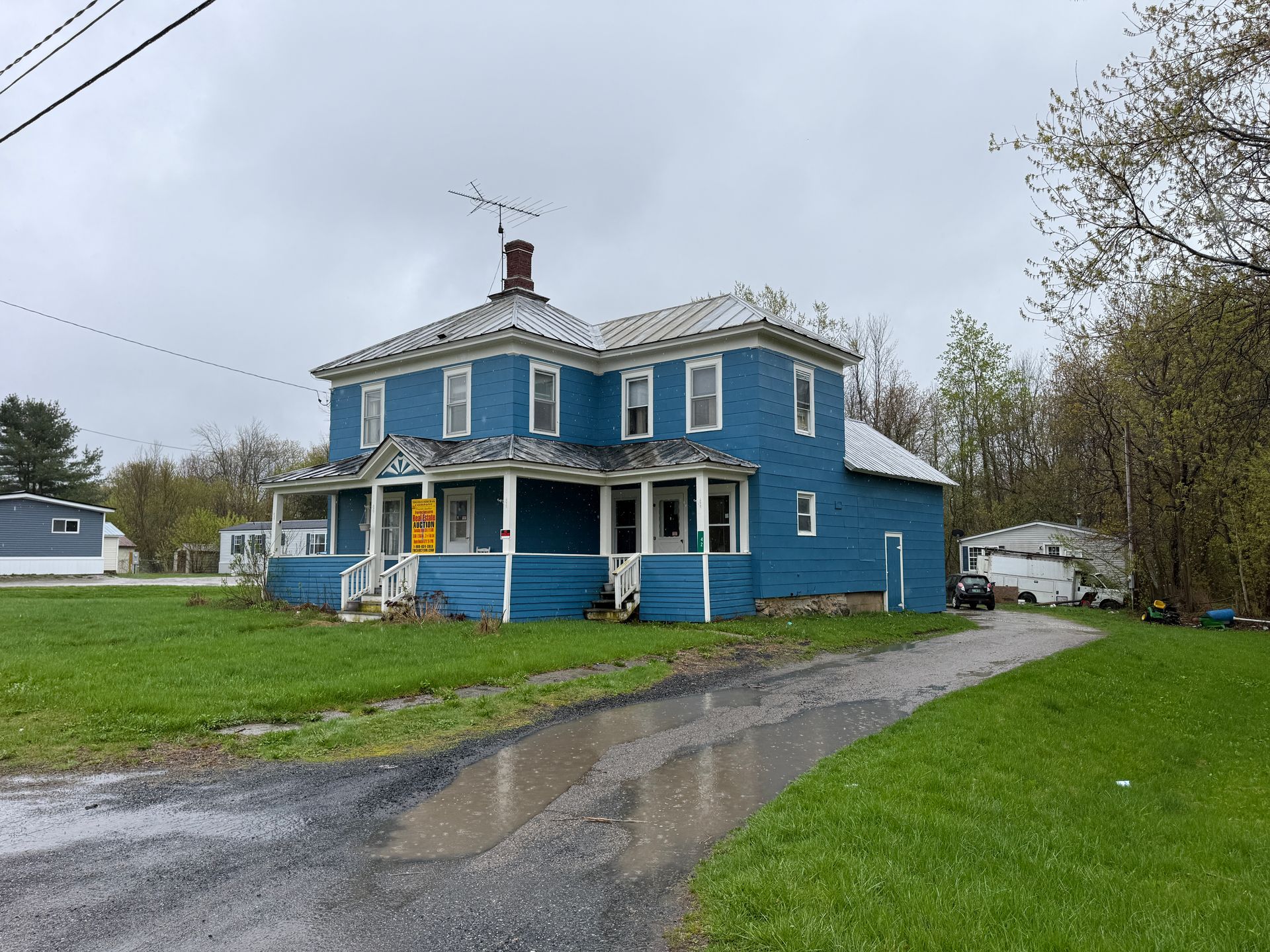 Blue two-story house with white trim beside a gravel driveway on a cloudy day