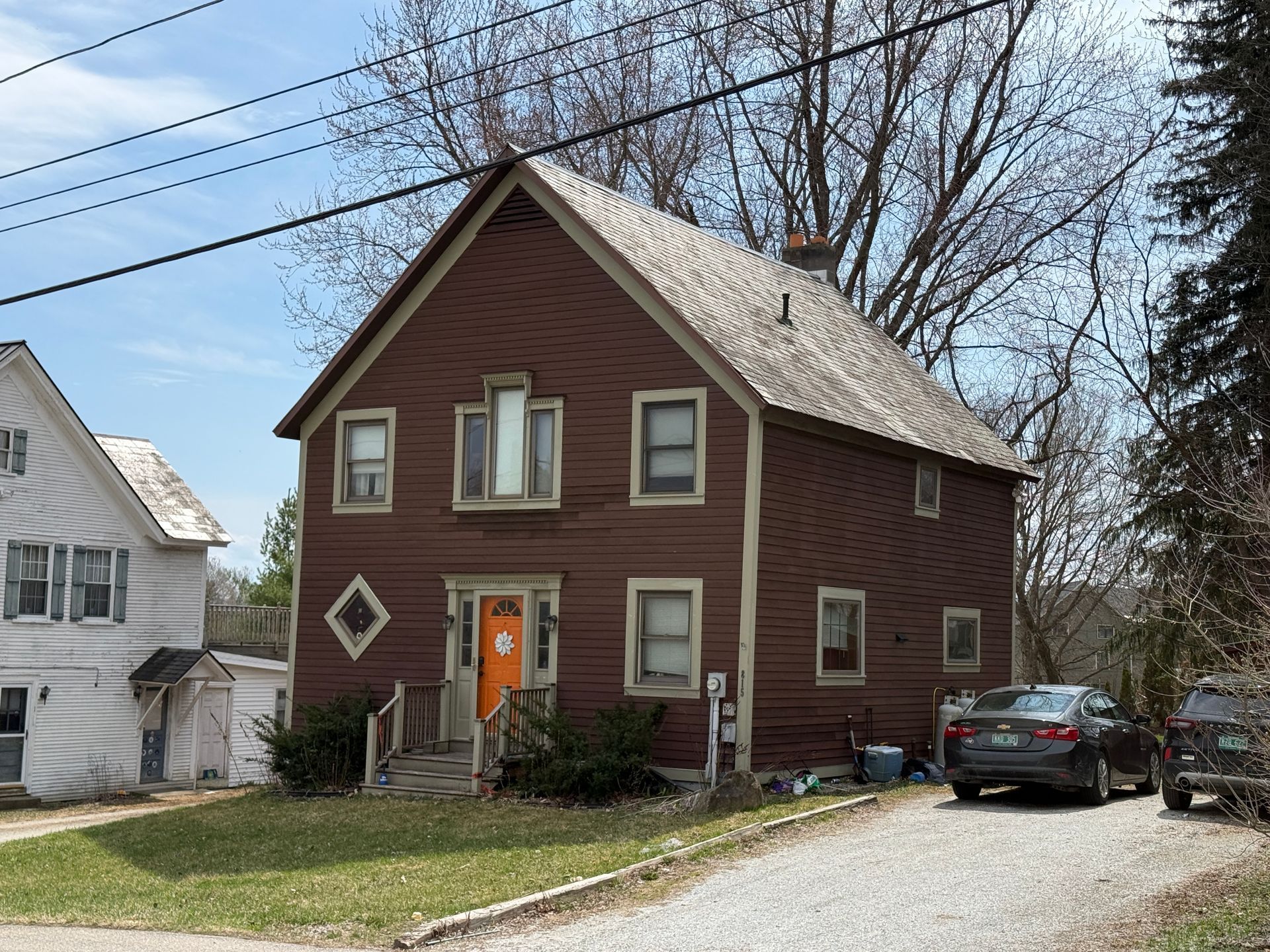 Brown two-story house with an orange door, parked car, and trees by the street.
