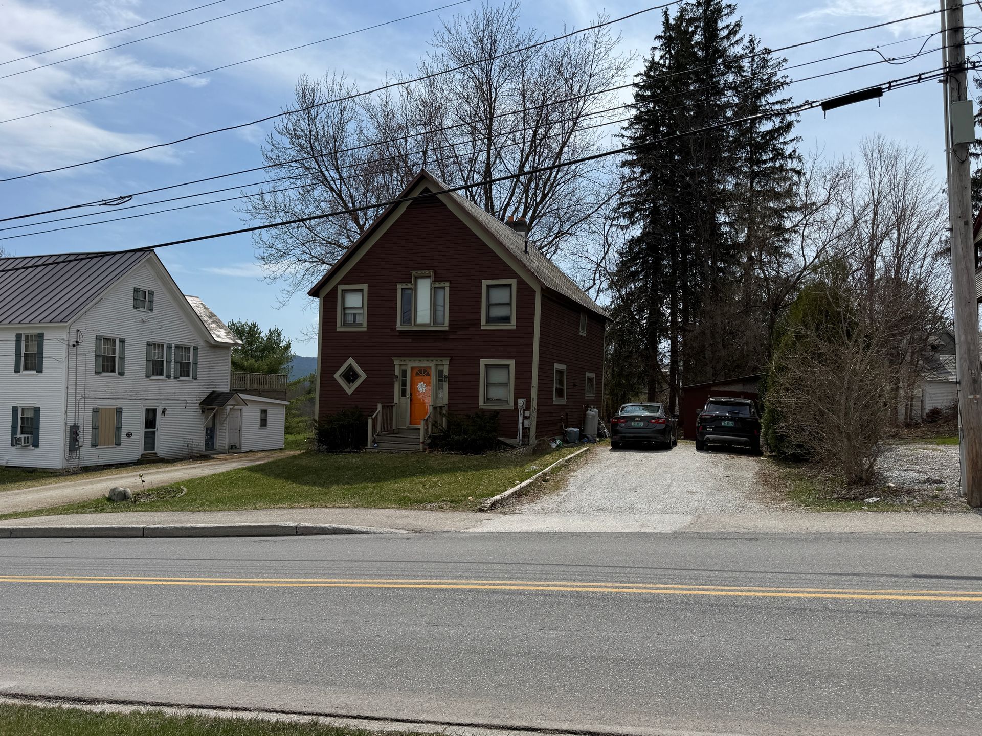 Red two-story house beside a road, with a gravel driveway and trees behind it.