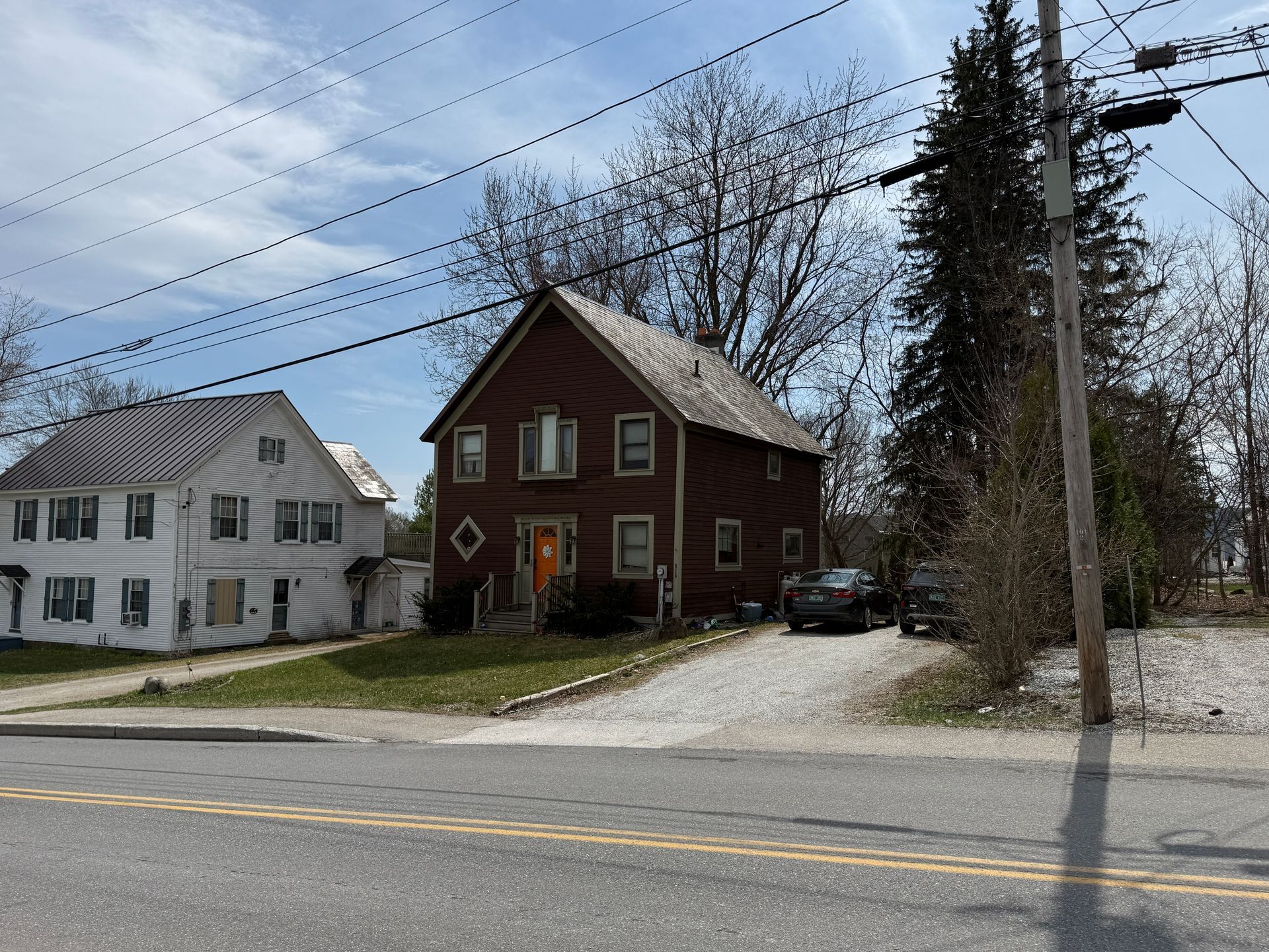 Red house and white house along a roadside under a cloudy sky, with power lines overhead.