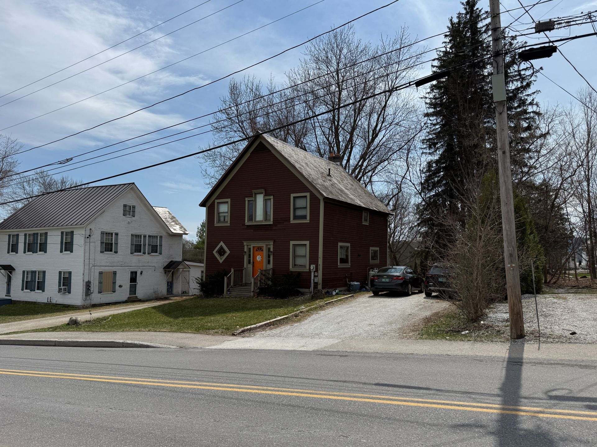 Red house and white house along a roadside under a partly cloudy sky, with power lines overhead.