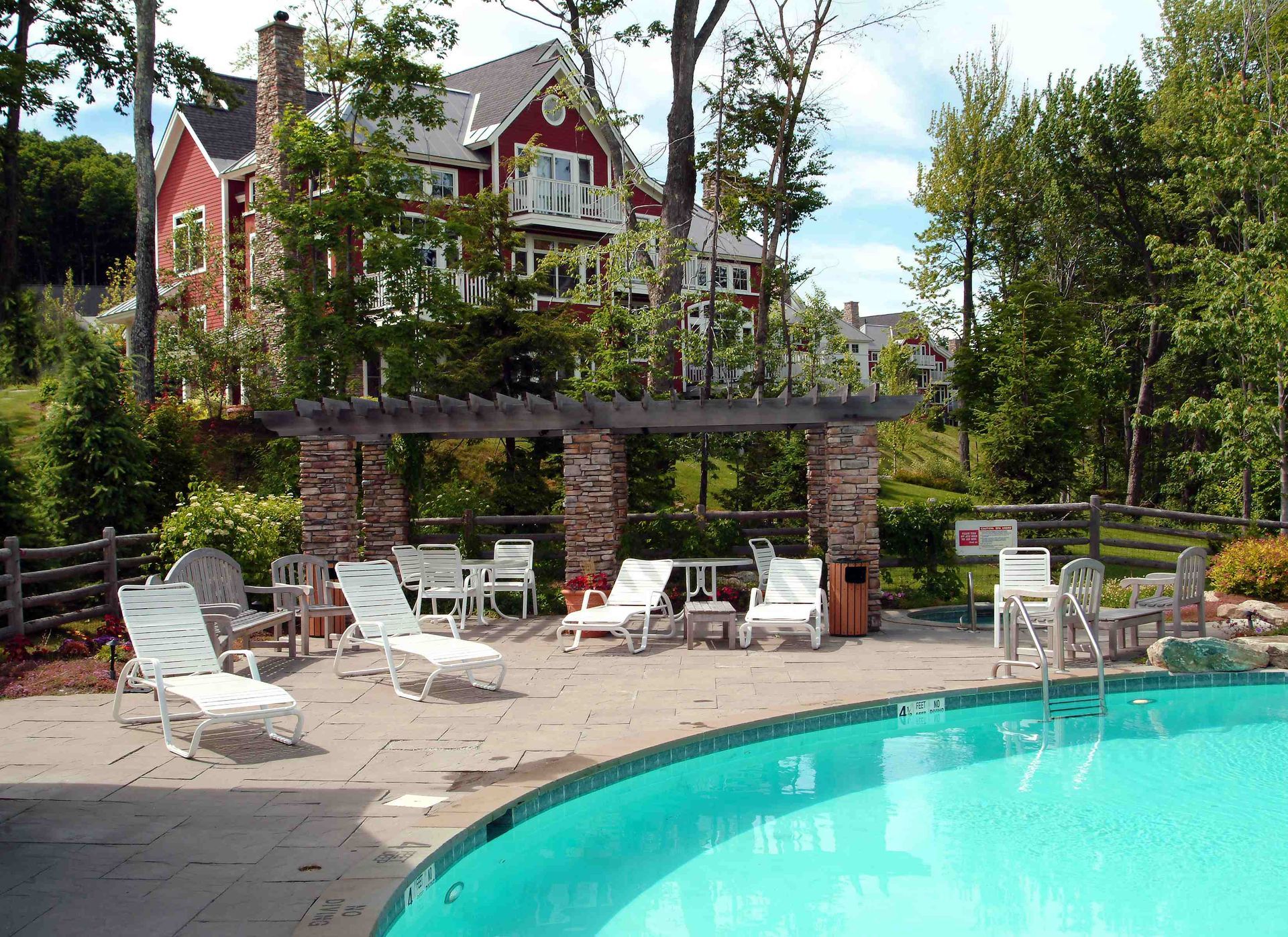 Pool area with lounge chairs, pergola, and red house in the background.