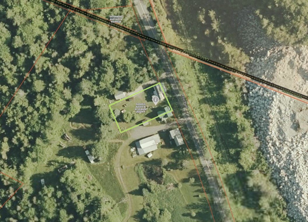 Aerial view of a rural property with a house, outbuildings, trees, and a road