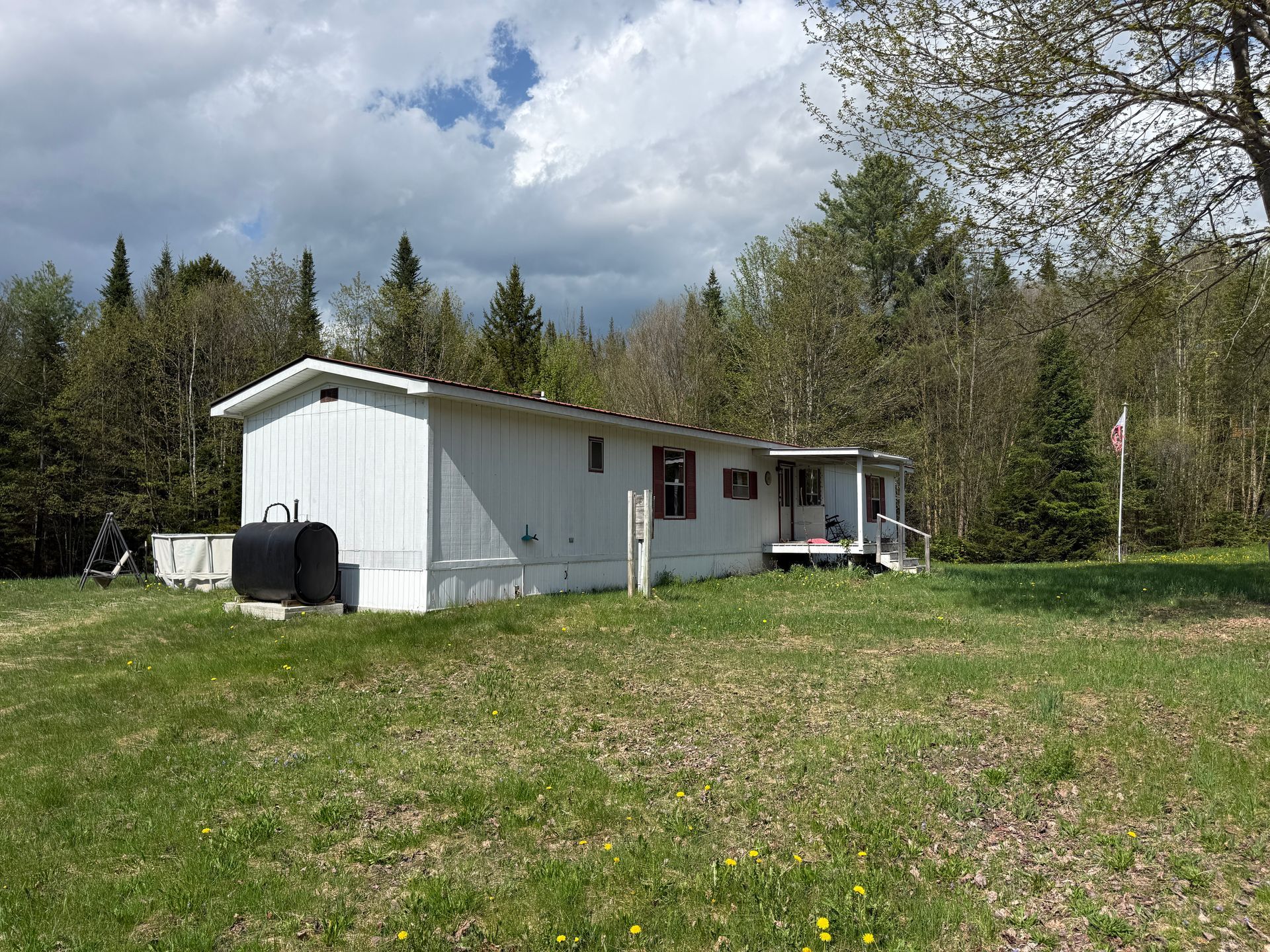 White cabin in a grassy field beside trees under a cloudy sky