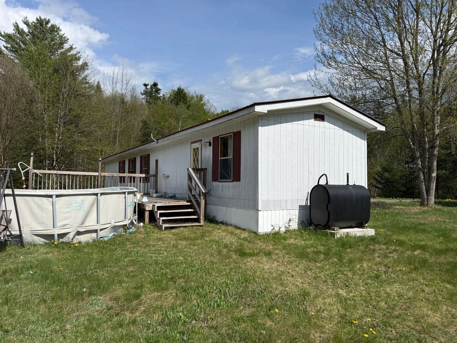 White mobile home in a grassy yard with steps, a porch, and trees under a blue sky