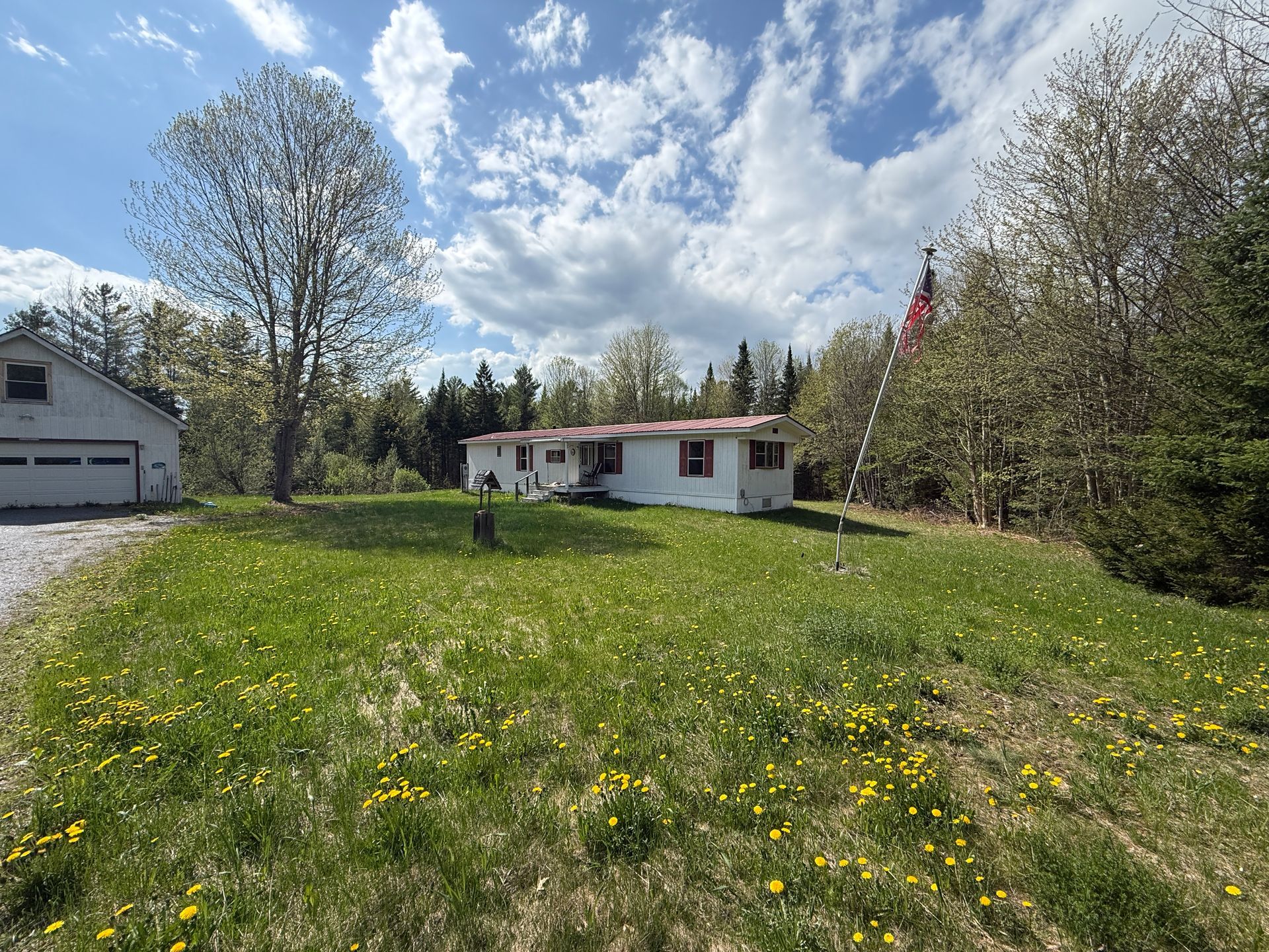 Rural house with white siding and red trim on a grassy lawn under a cloudy blue sky