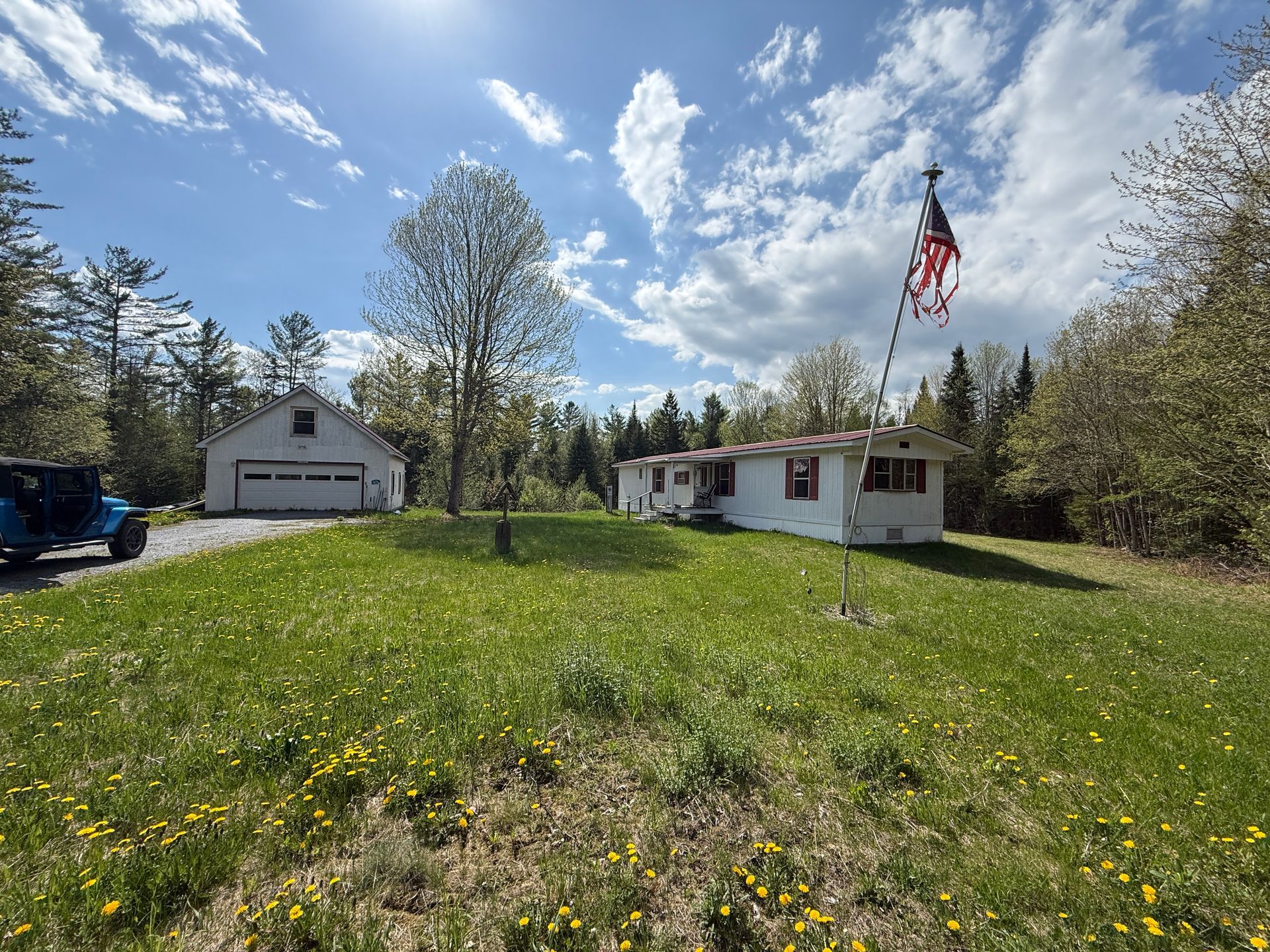 Grassy yard with a white house, garage, and American flag under a partly cloudy blue sky