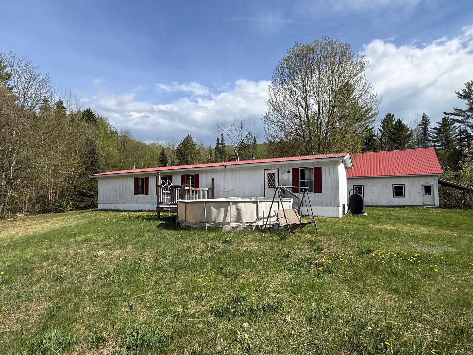 Small white house with red roof and porch, set in a grassy yard under a partly cloudy sky.