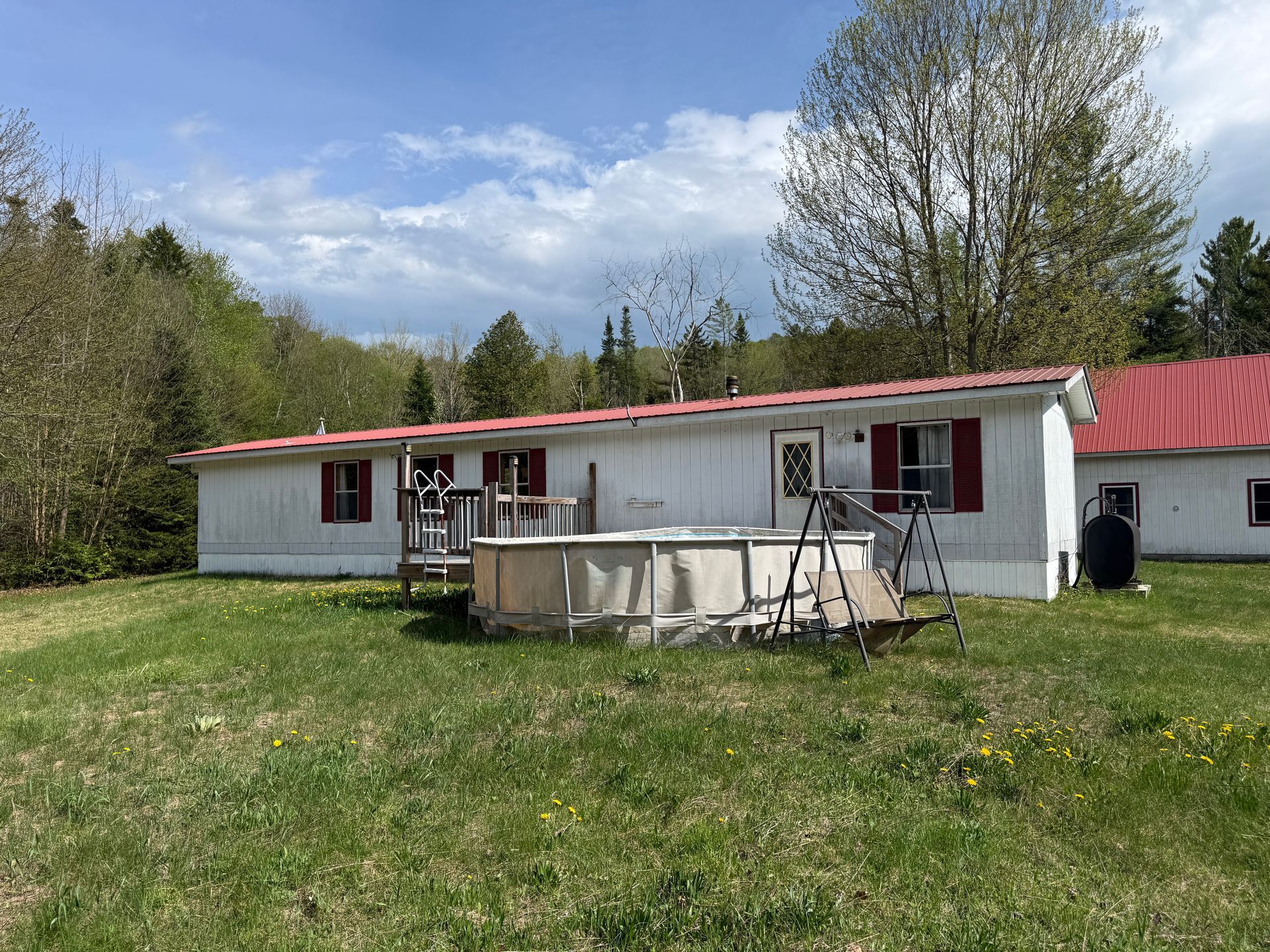 Rural house with red roof, grassy yard, and trees under a partly cloudy sky