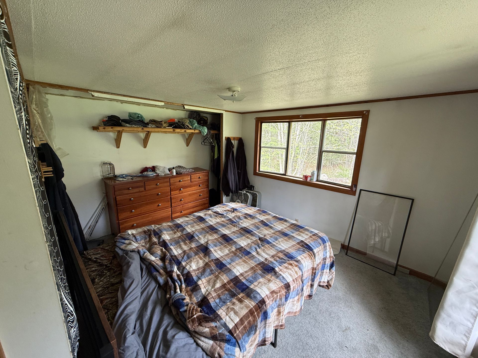 Bedroom with a plaid bedspread, wooden dresser, and sunlit window.