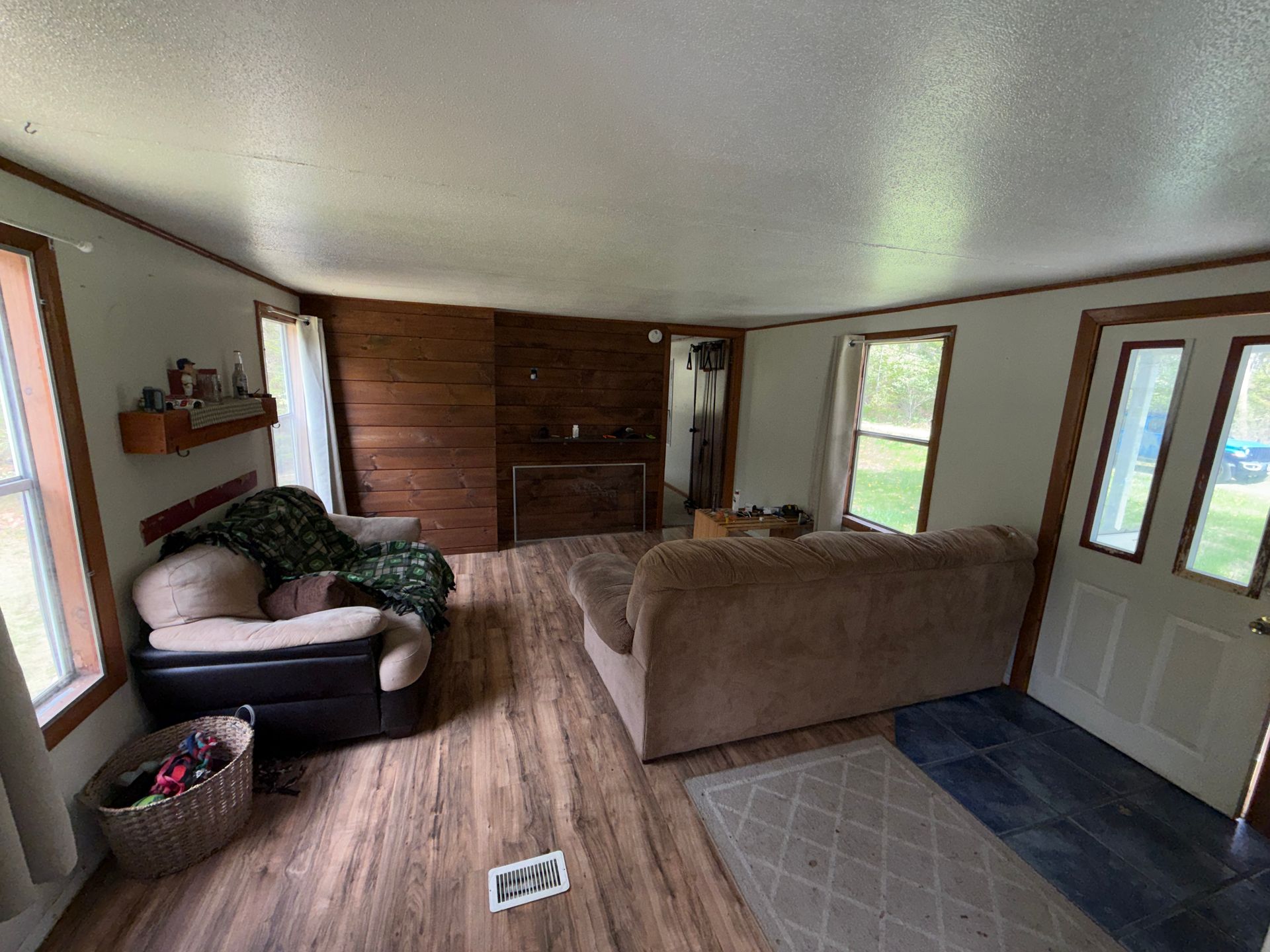 Living room with tan couch, chair, wood floor, front door, and windows casting daylight