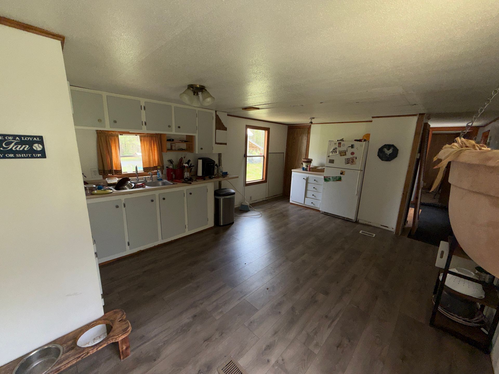 Open kitchen and living area with white cabinets, wood floors, and a window above the sink