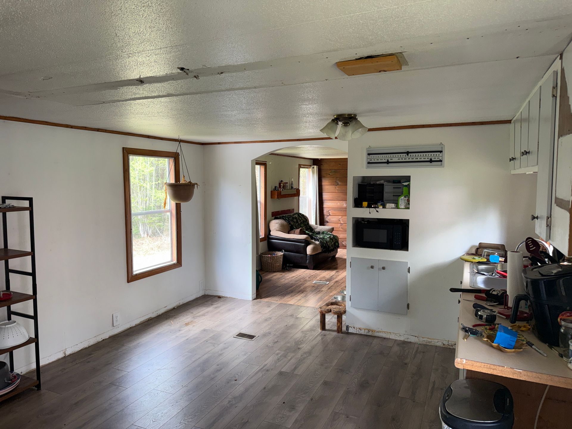 Sparse living room with white walls, wood floor, window, doorway, and a TV on a stand against the right wall