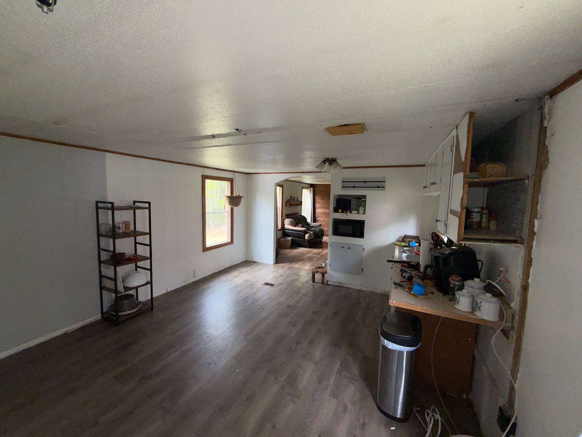 Empty living room with gray floors, white walls, a window, shelving, and a small kitchenette area.
