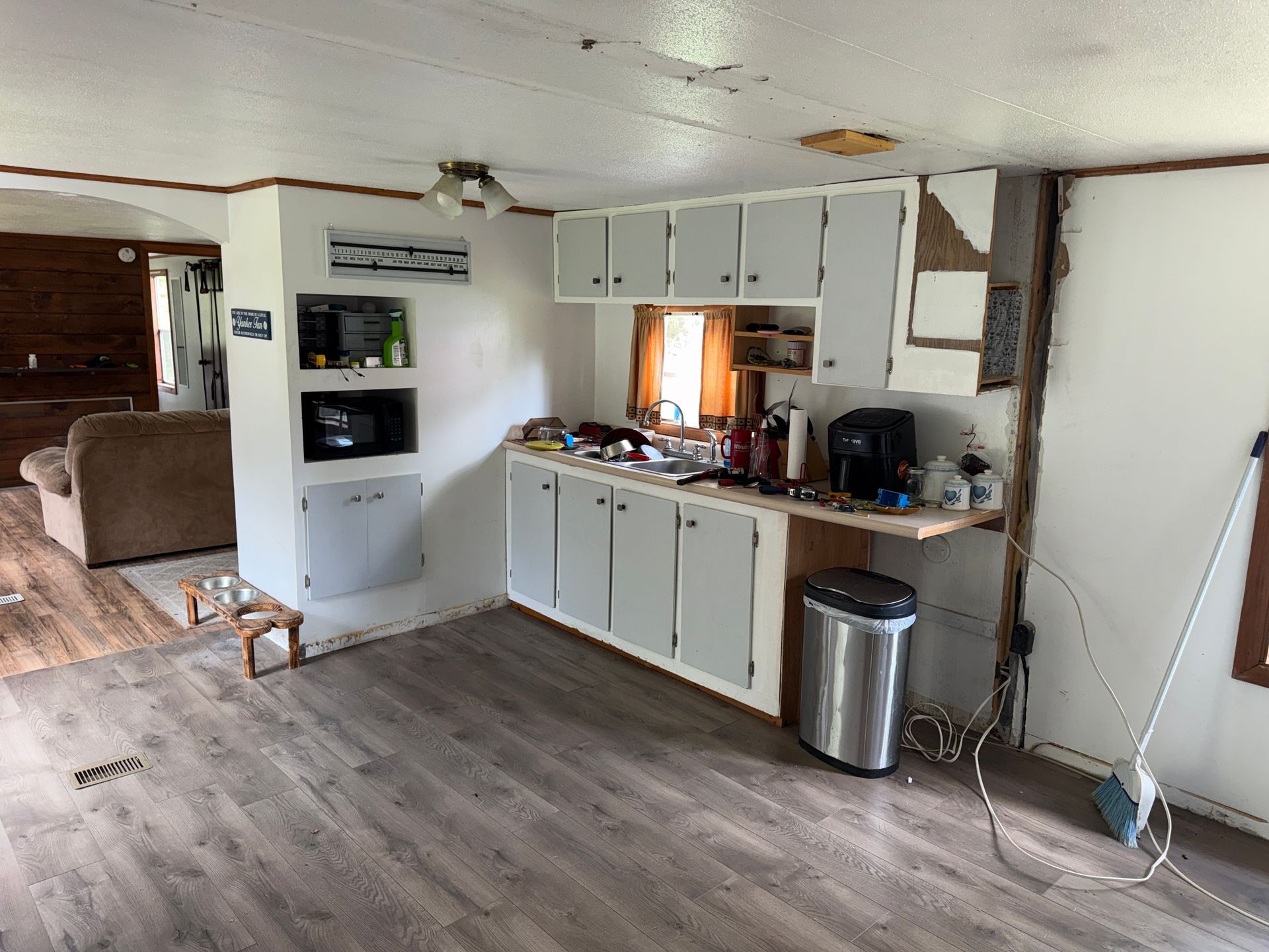 Kitchen with white cabinets, wood counters, trash can, and open living room beyond.
