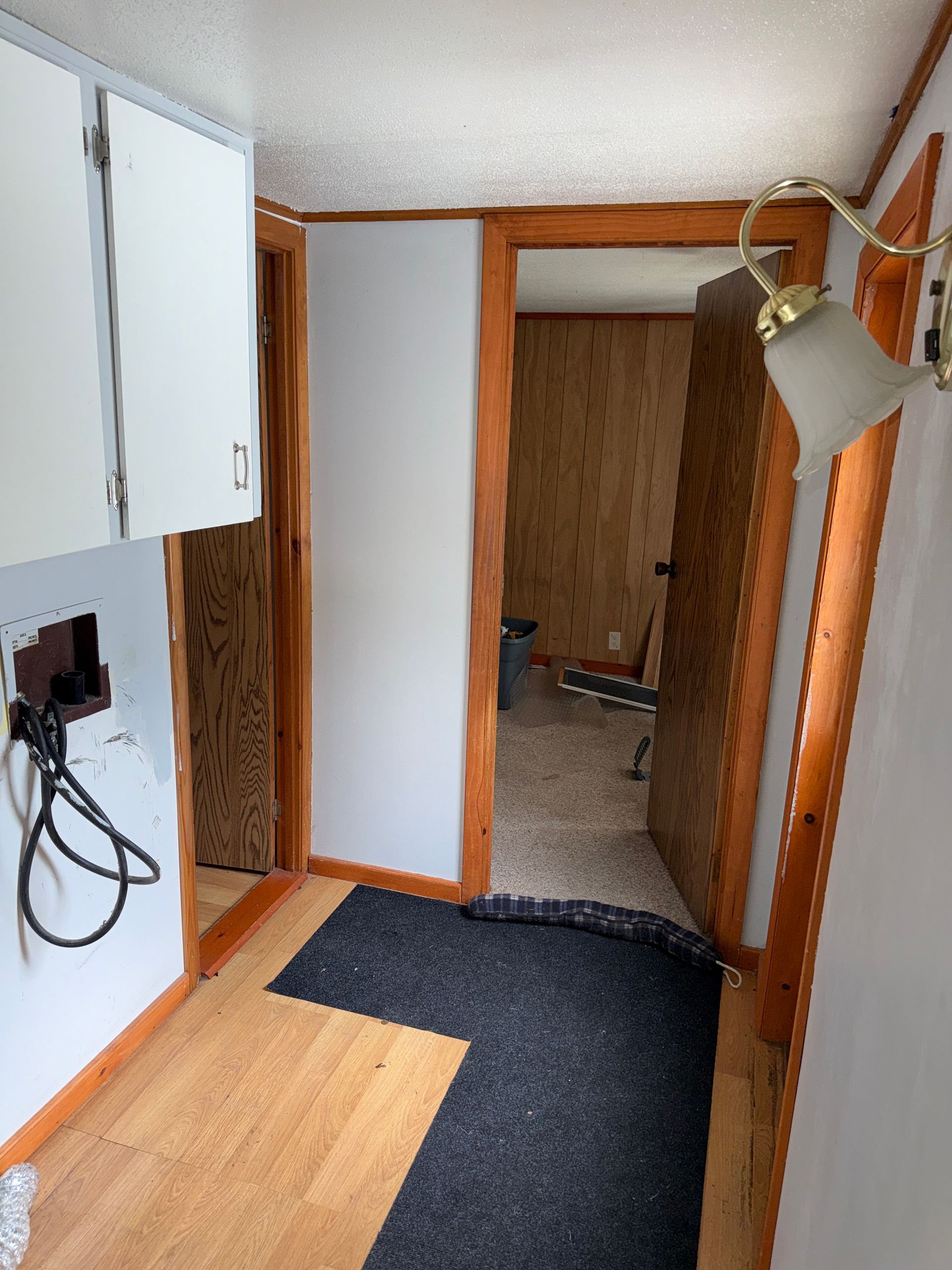 Narrow hallway with white cabinets, wood trim, dark floor mats, and an open doorway