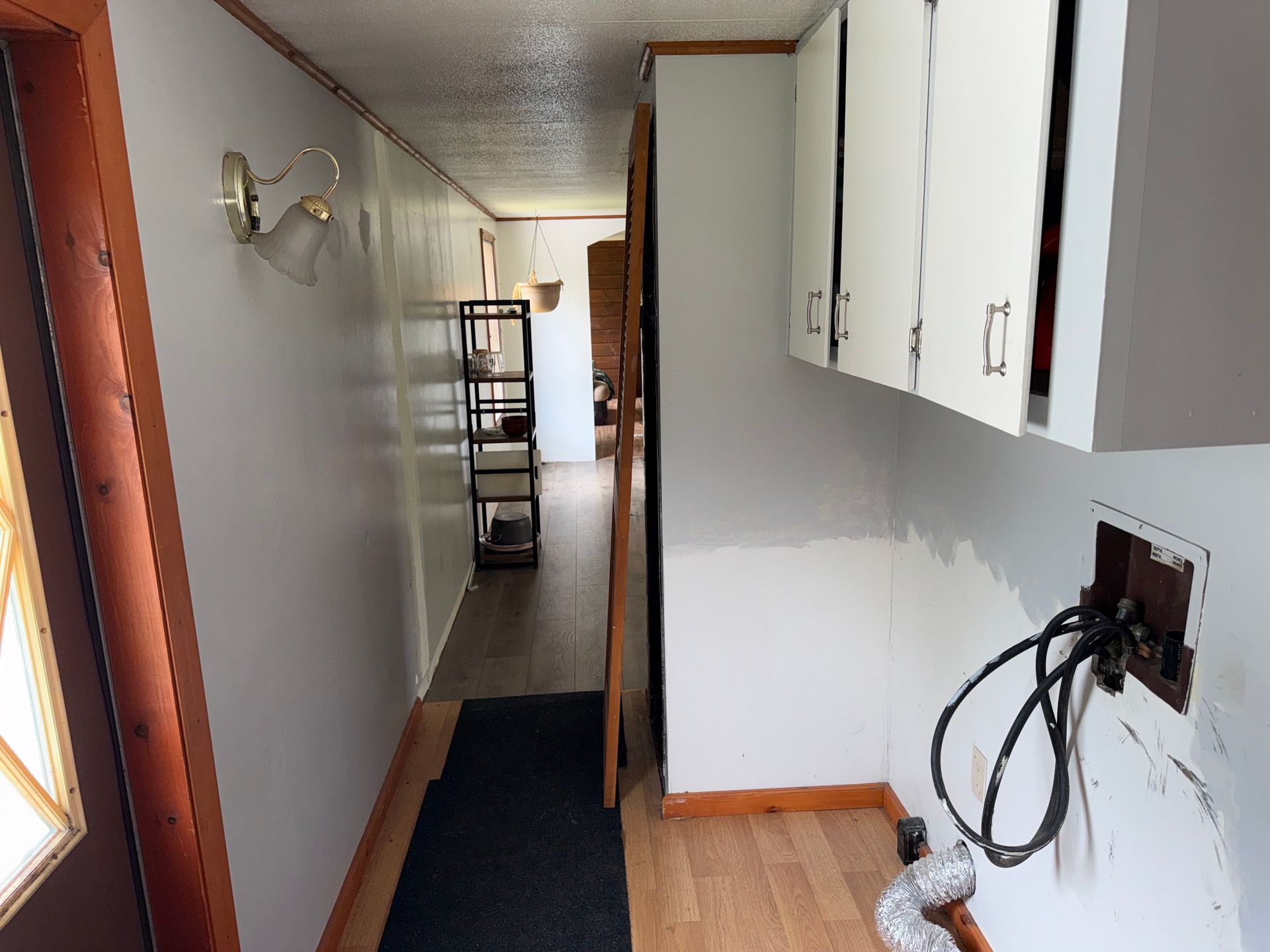 Narrow hallway with white cabinets, dark runner rug, and a wall-mounted light.