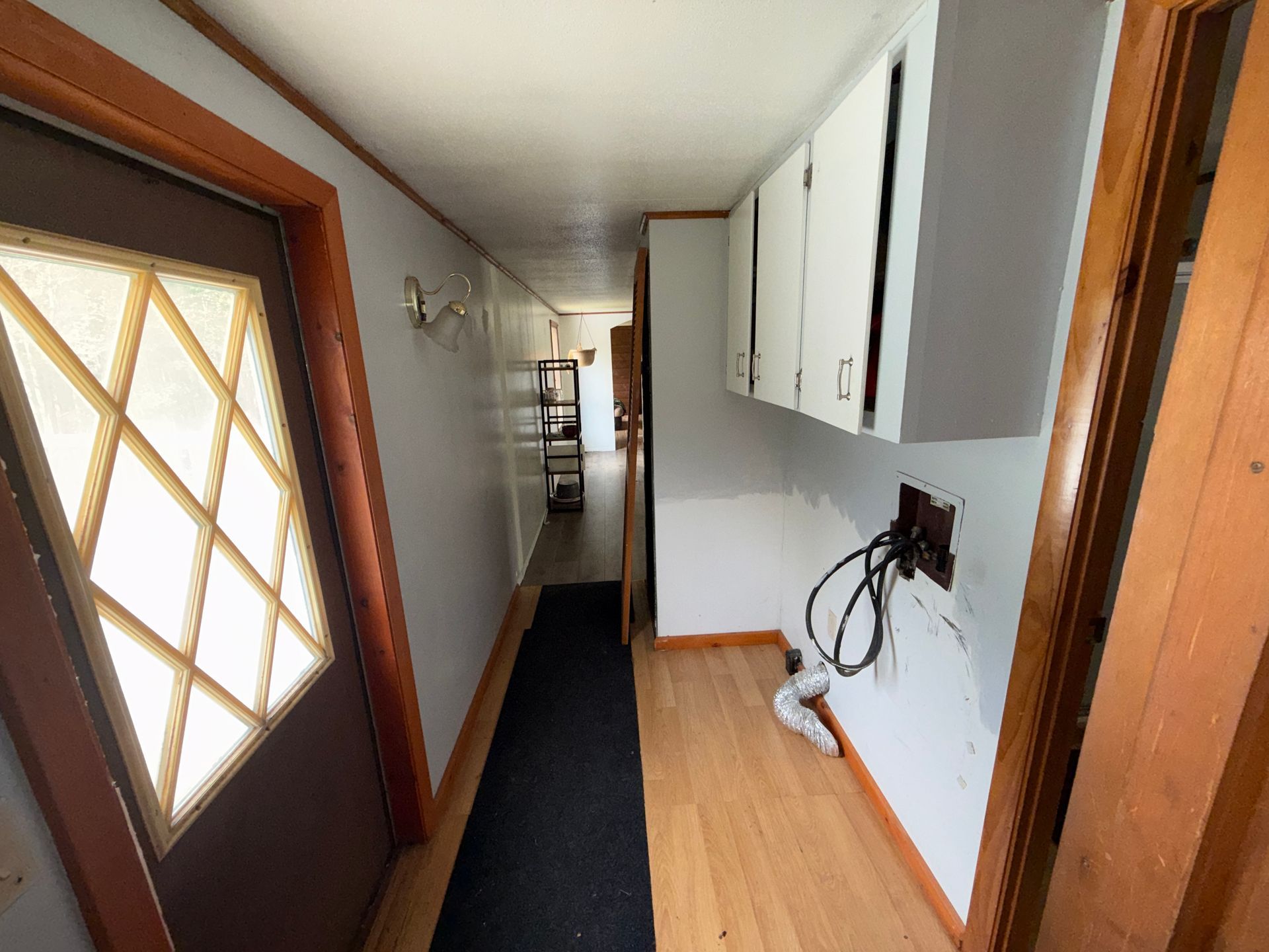 Narrow hallway with a brown door, black runner, white cabinets