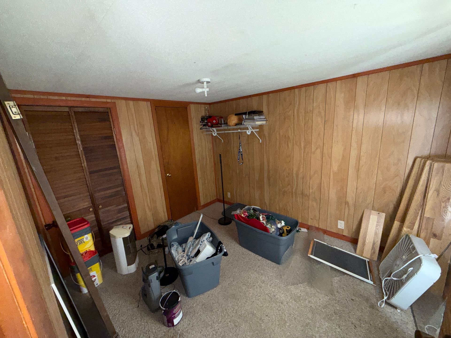 Basement room with wood-paneled walls, bins, tools, and boards