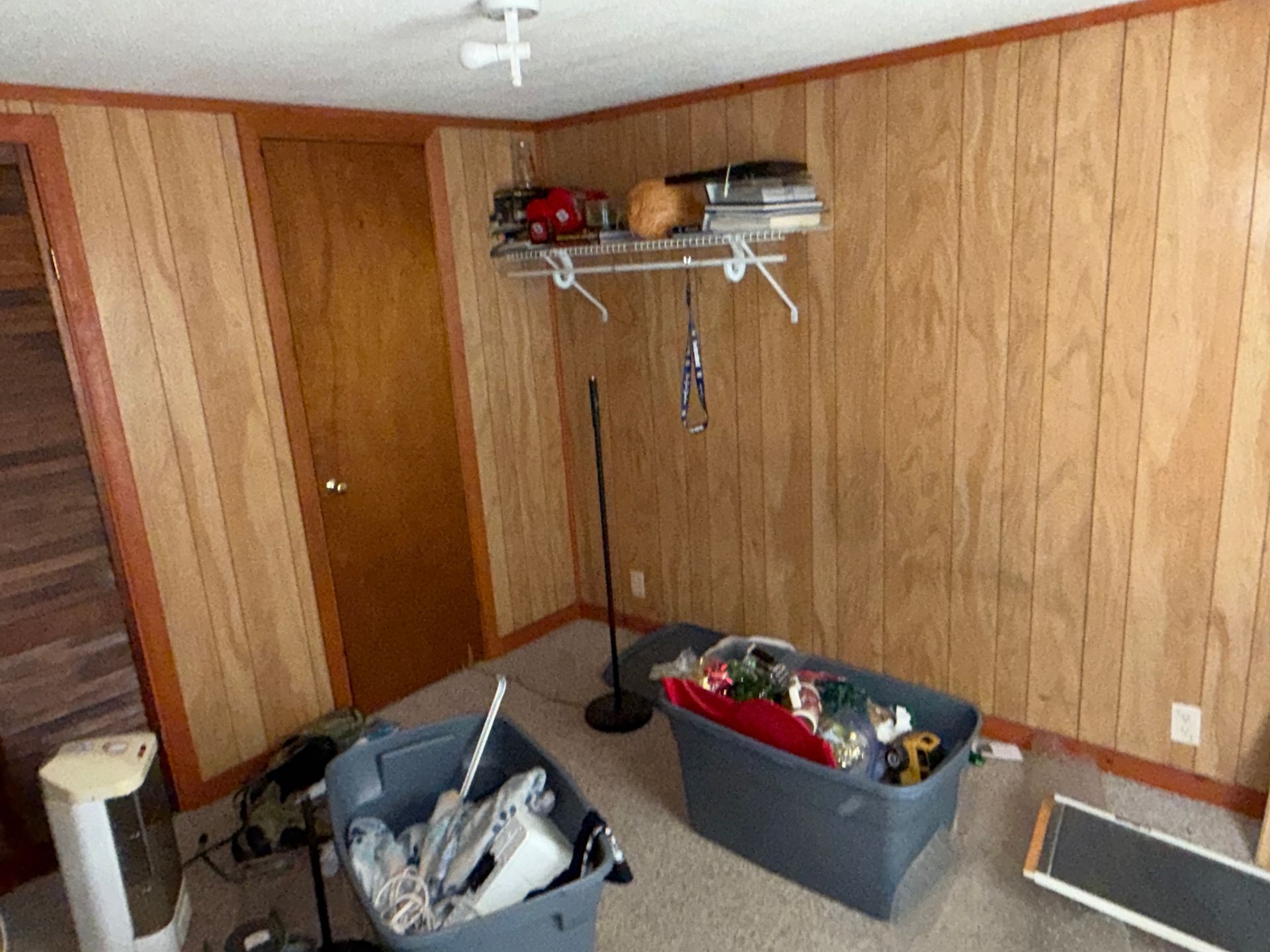 Wood-paneled basement room with storage bins, shelves, and a folded exercise machine.