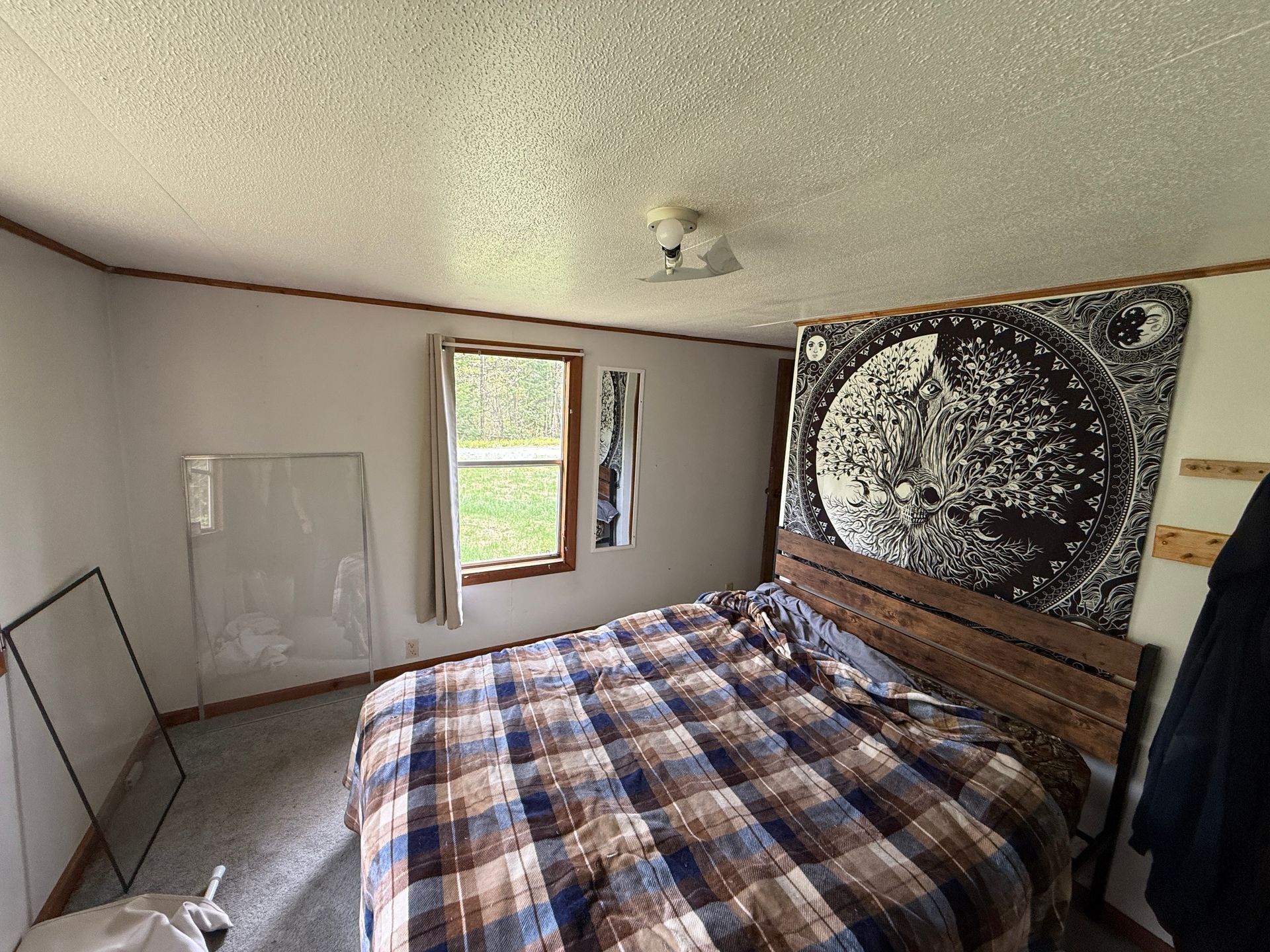 Cozy bedroom with plaid bedspread, tapestry wall hanging, window, and leaning mirror