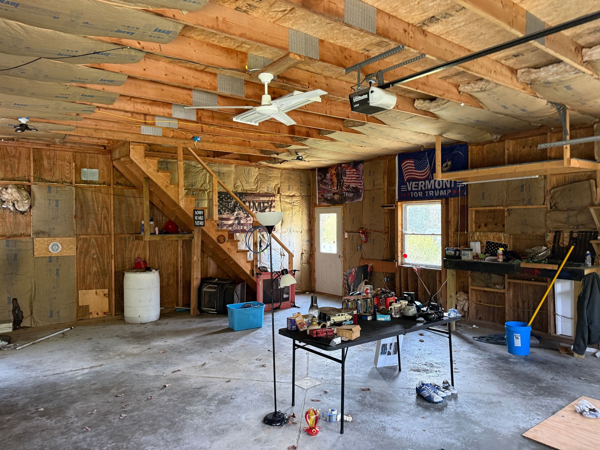 Garage with exposed rafters, tools, and a worktable under bright windows