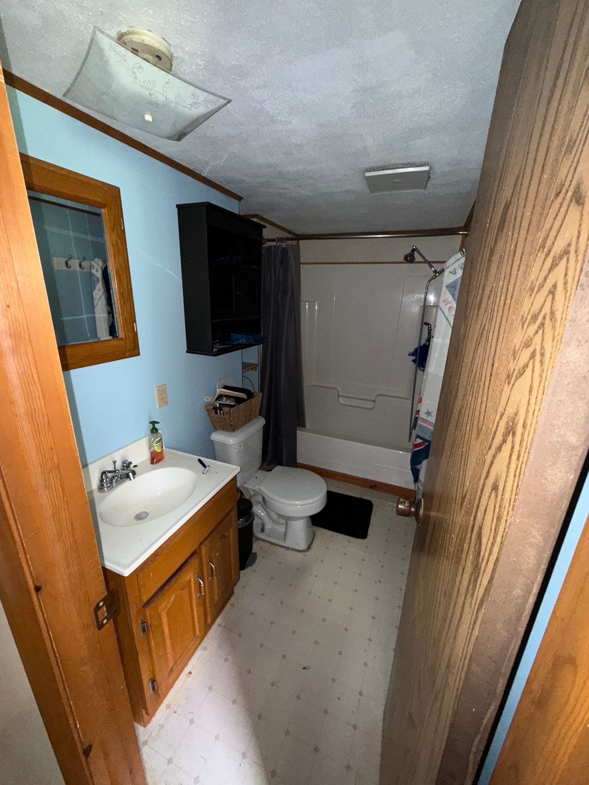 Small bathroom with wood vanity, toilet, shower curtain