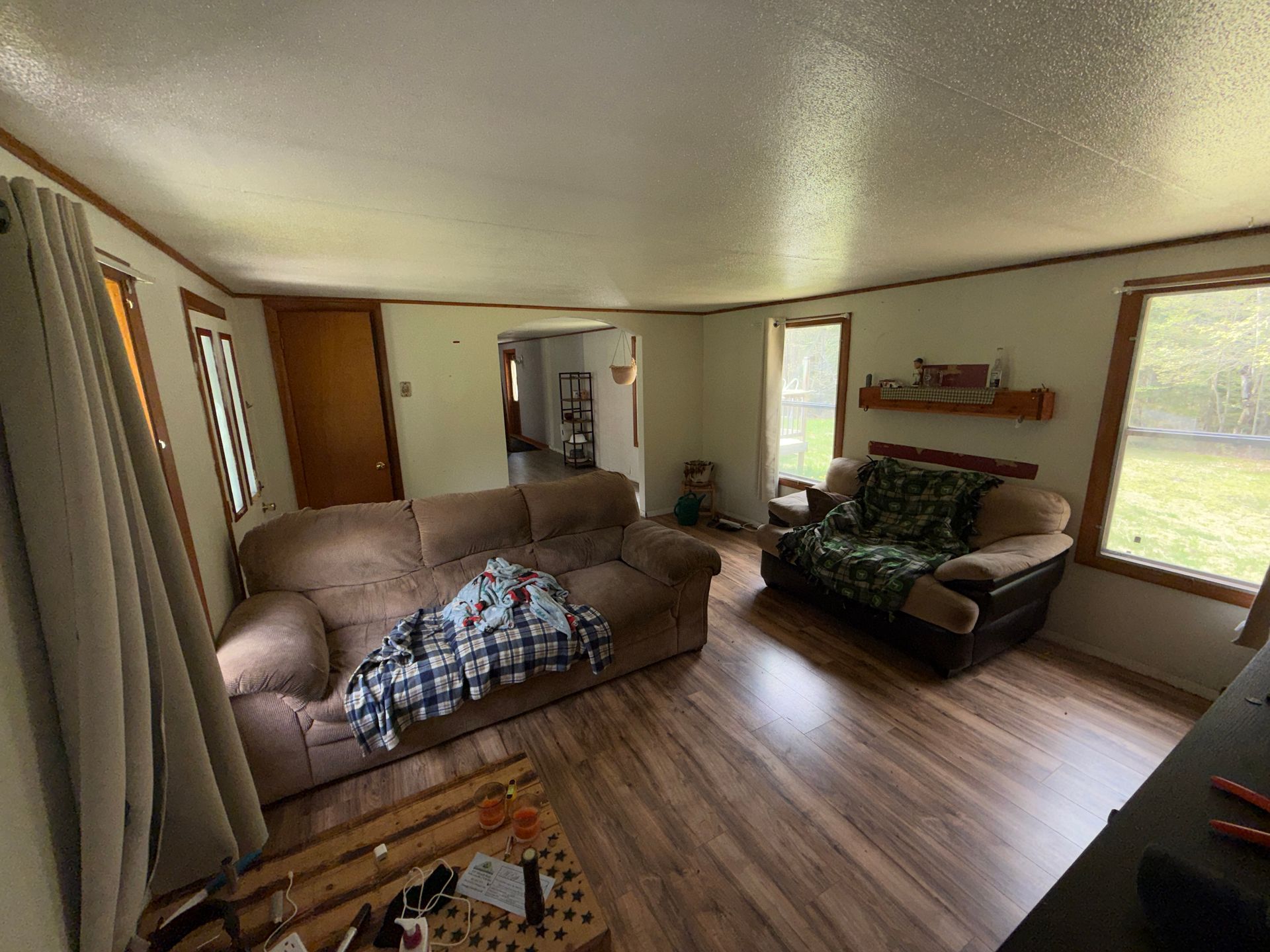 Bright living room with beige sectional, brown sofa, wood floors, large windows, and wall shelves