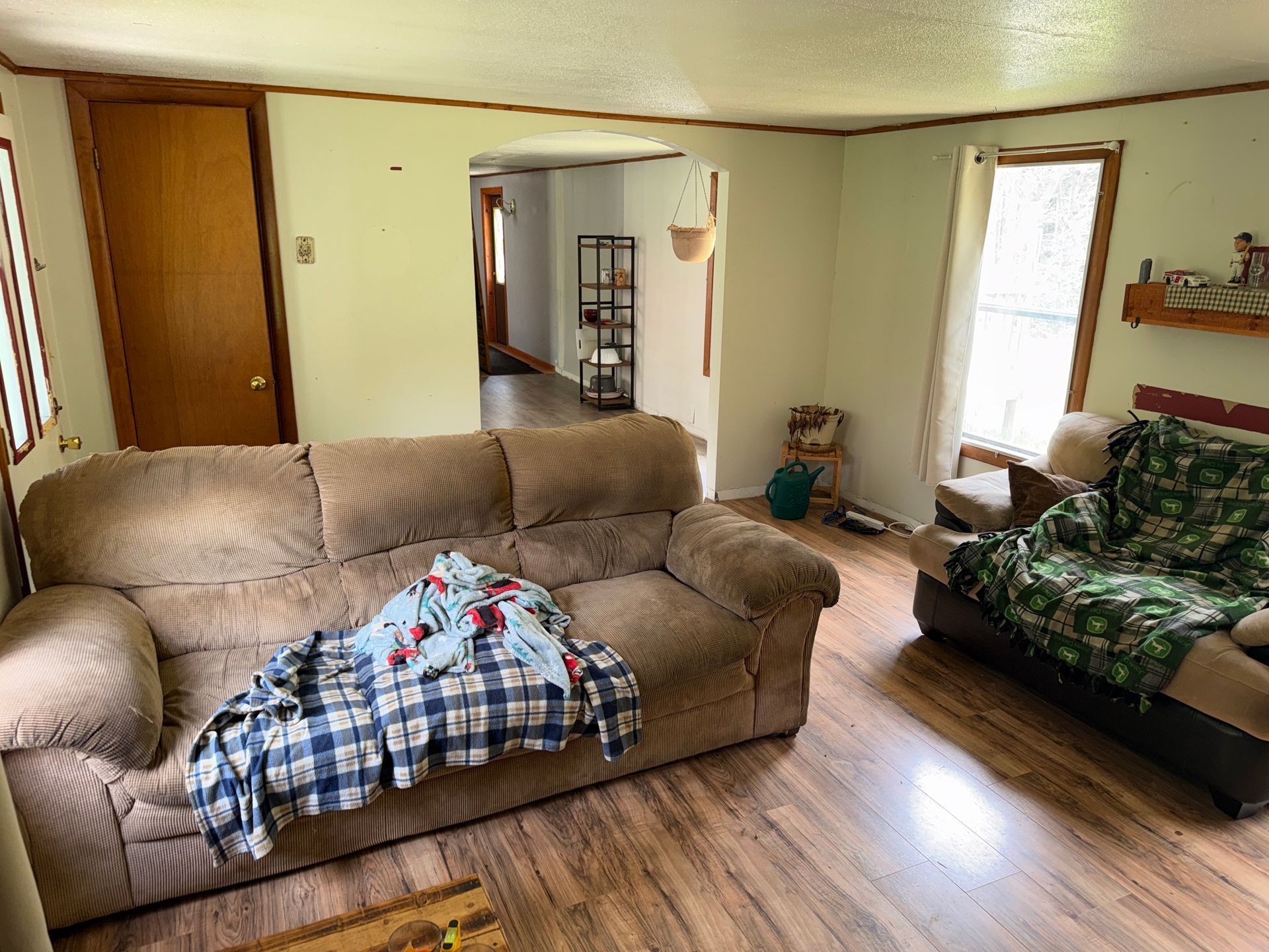 Living room with tan couch, green chair, wooden floors, and a blanket draped over the sofa